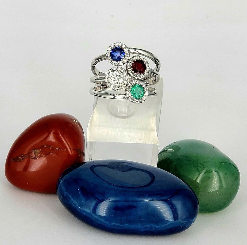 Pila di anelli con pietre preziose su un supporto trasparente, con quattro pietre colorate lucidate nella parte anteriore.