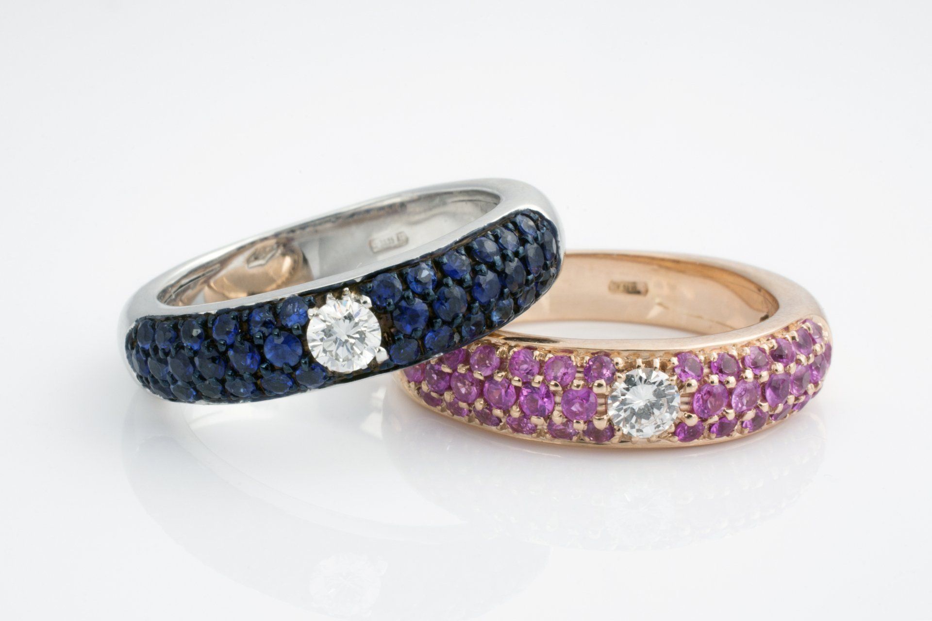 Due anelli: uno in argento con gemme blu, l'altro in oro con gemme rosa, entrambi con un diamante centrale.