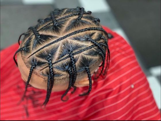 The back of a person 's head with braids and a red shirt.