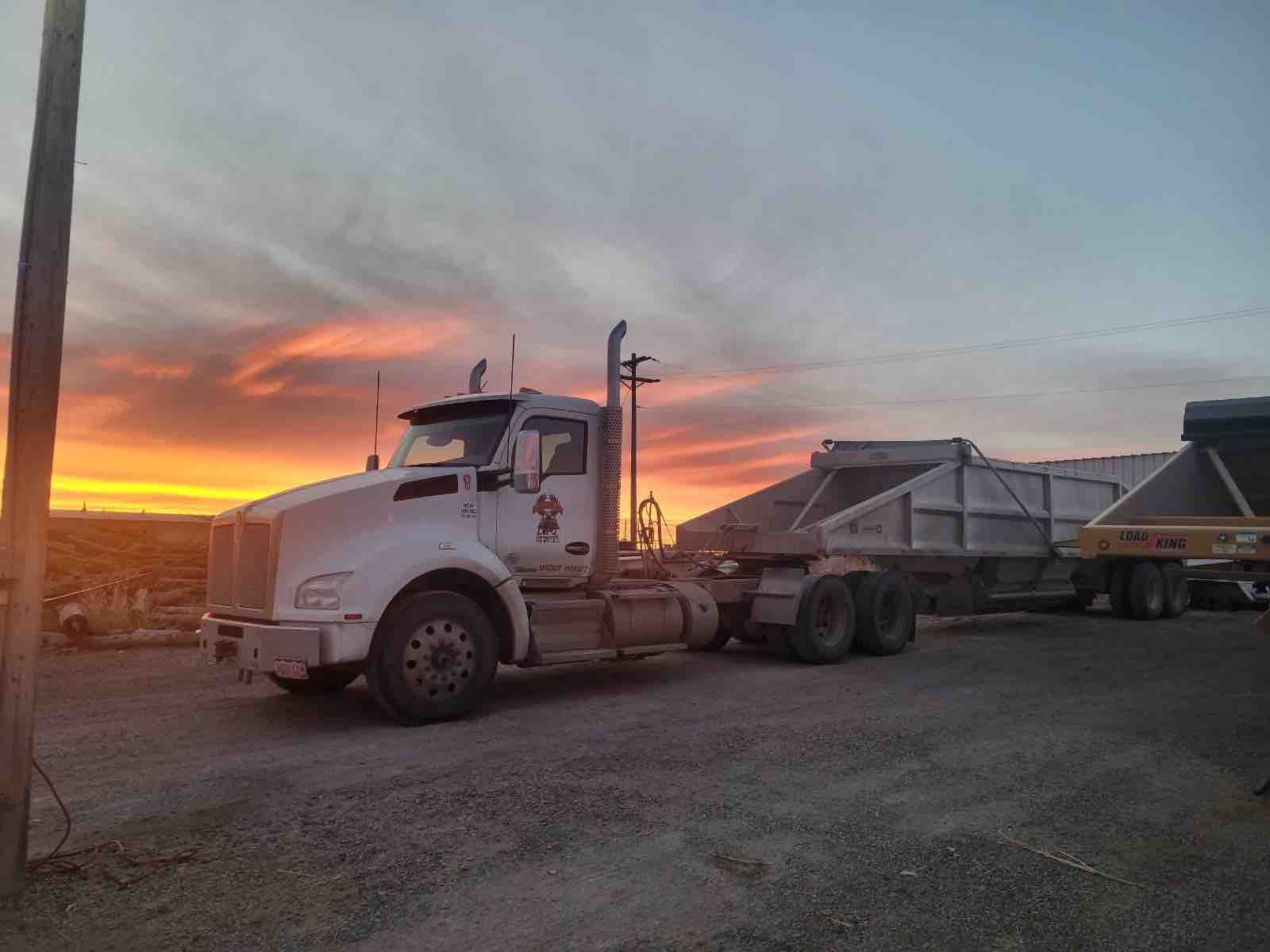 A semi truck is parked in a gravel lot at sunset.