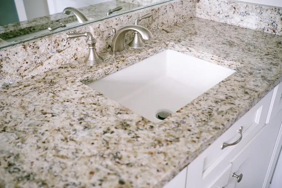 Bathroom vanity with granite countertop, white sink, and silver faucet.
