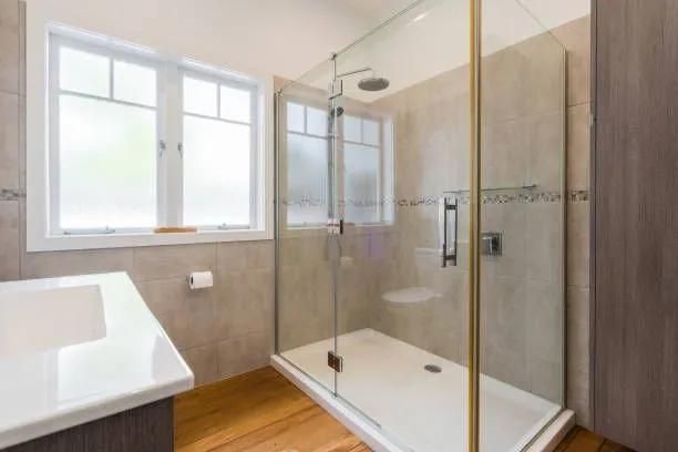 Bathroom with a glass shower, white vanity, and a window. Beige tiled walls and light wood floor.