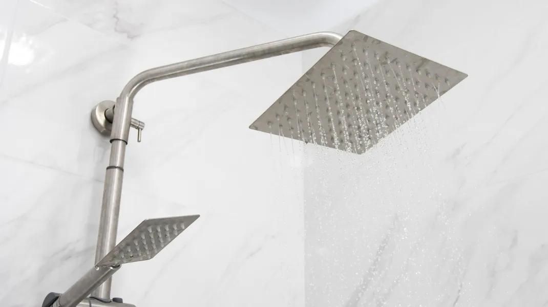 Shower head with water spraying; stainless steel, against white marble tile.