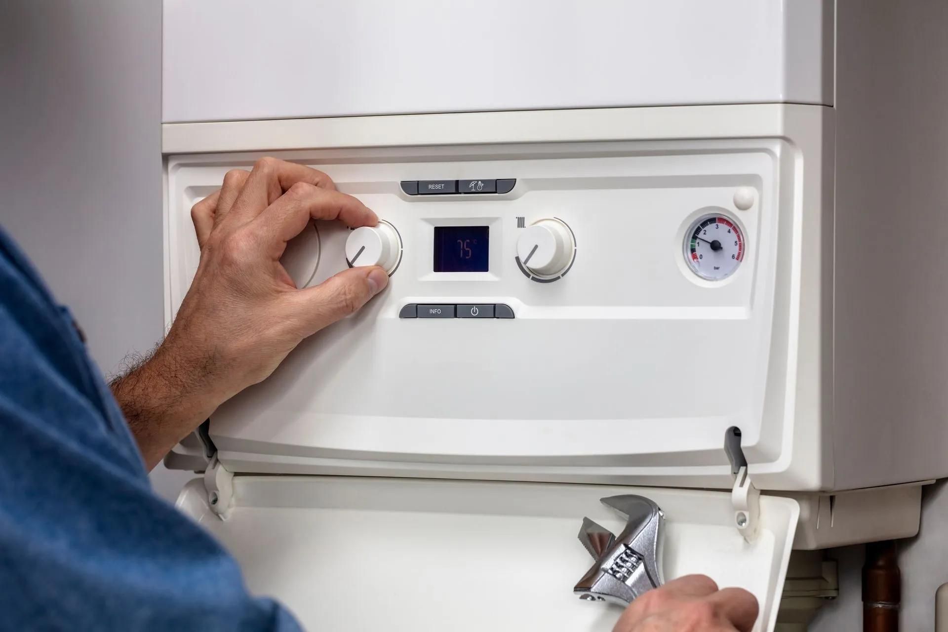 Person adjusting a white boiler control dial with a wrench in the open panel, indoors.