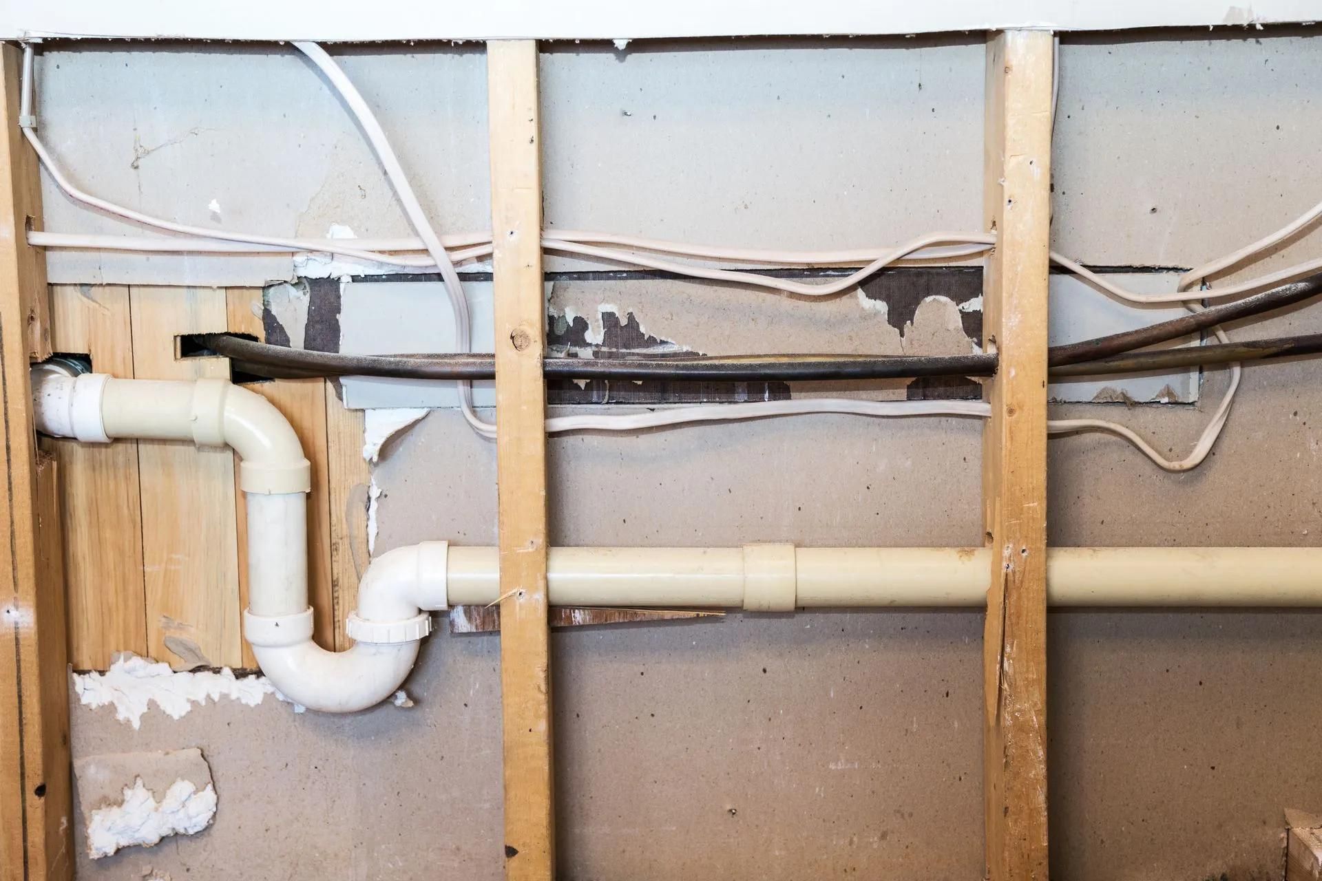 Framing of wall with exposed plumbing pipes and electrical wiring.