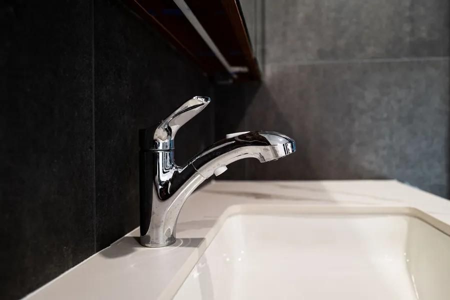 Chrome faucet over a white sink in a bathroom. Dark gray tiled wall in the background.