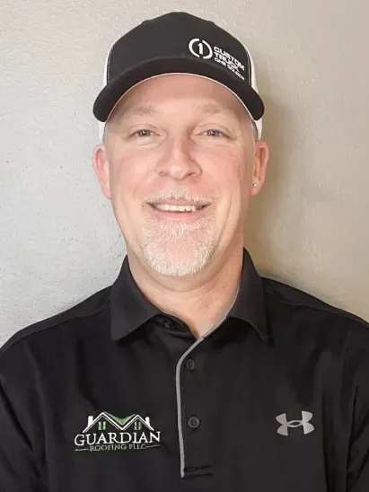 A headshot of a person with short dark hair, wearing a black polo shirt, centered against a plain gray background.