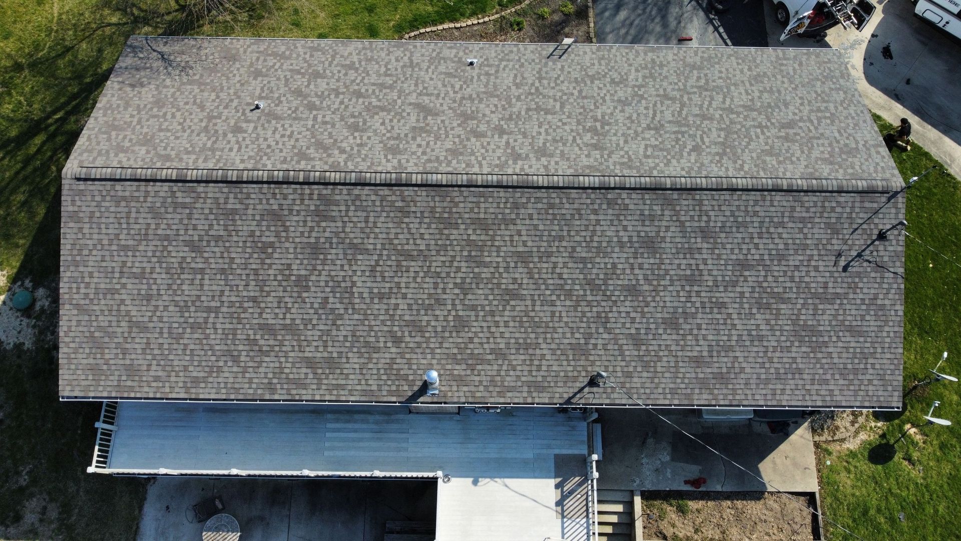 An aerial view of a rectangular brown shingled roof with two small vents above a white patio area.