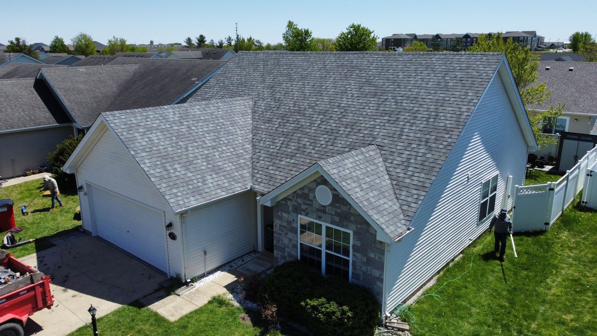 An aerial view of a single-story house with a new grey shingled roof, during a roof replacement project.