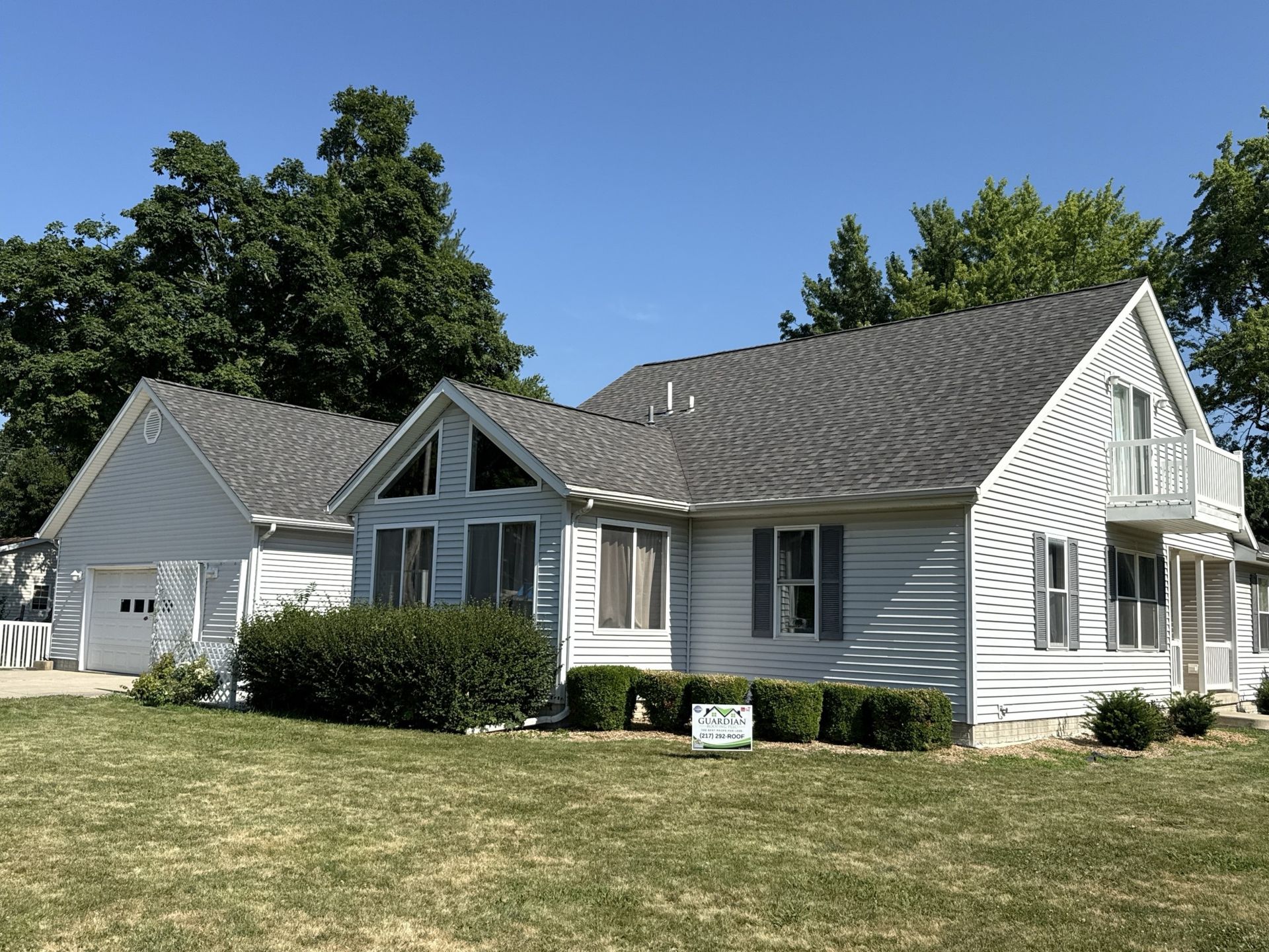 A white house with a gray roof and attached garage sits on a grassy lawn under a clear blue sky.