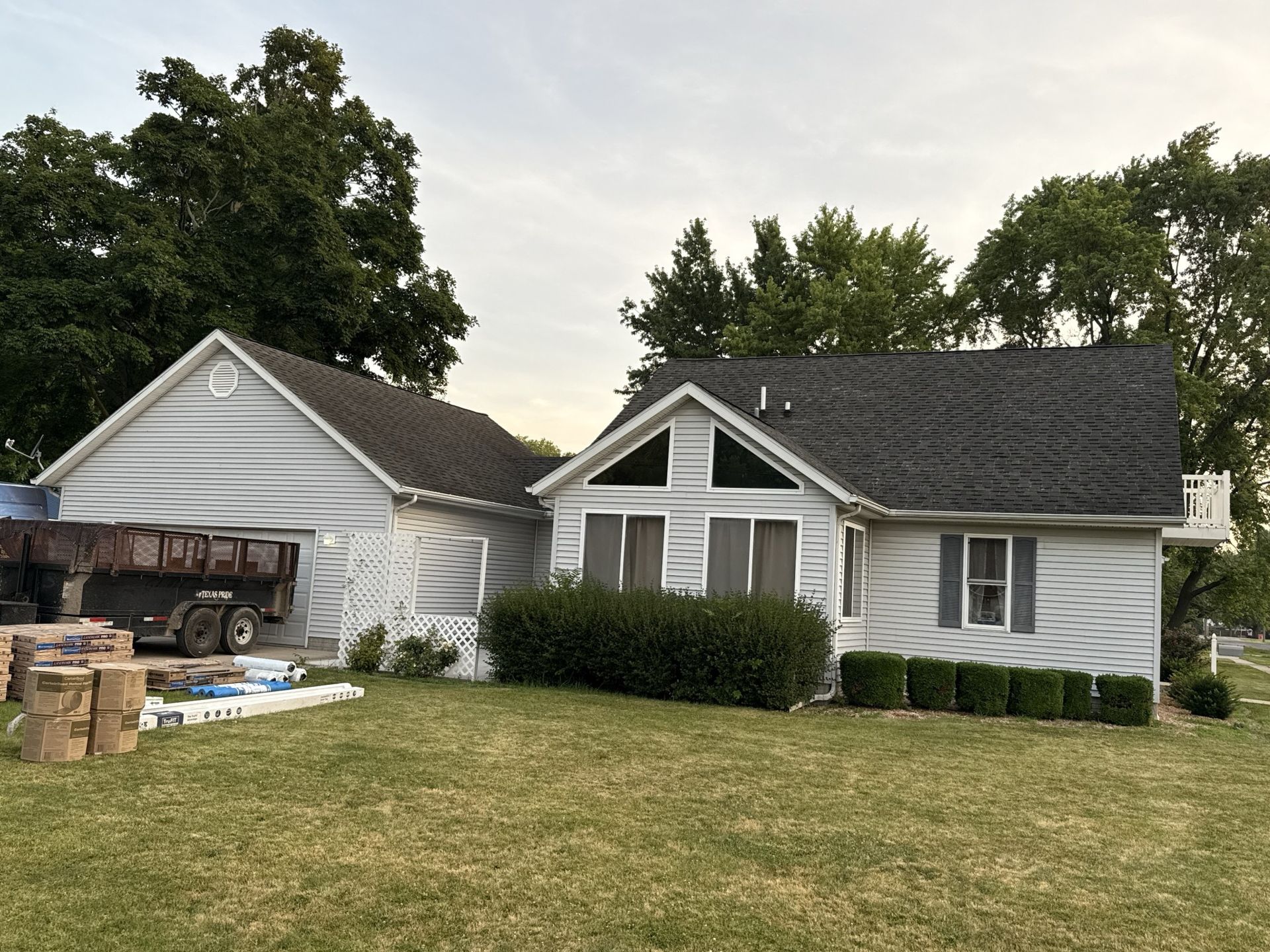 A light-gray home with a dark roof and large windows, featuring a construction dumpster and building materials nearby.
