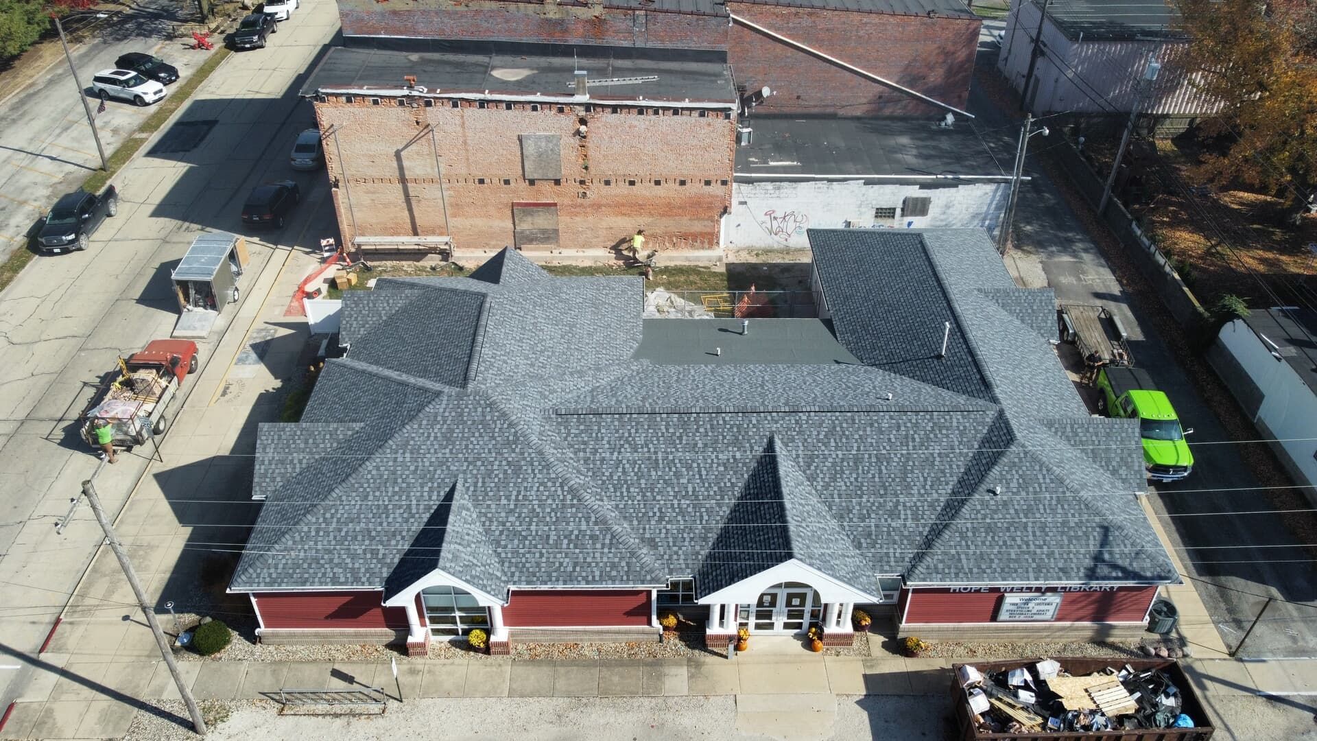 Aerial view of a red brick commercial building with a new gray shingled roof, situated next to a brown brick building.