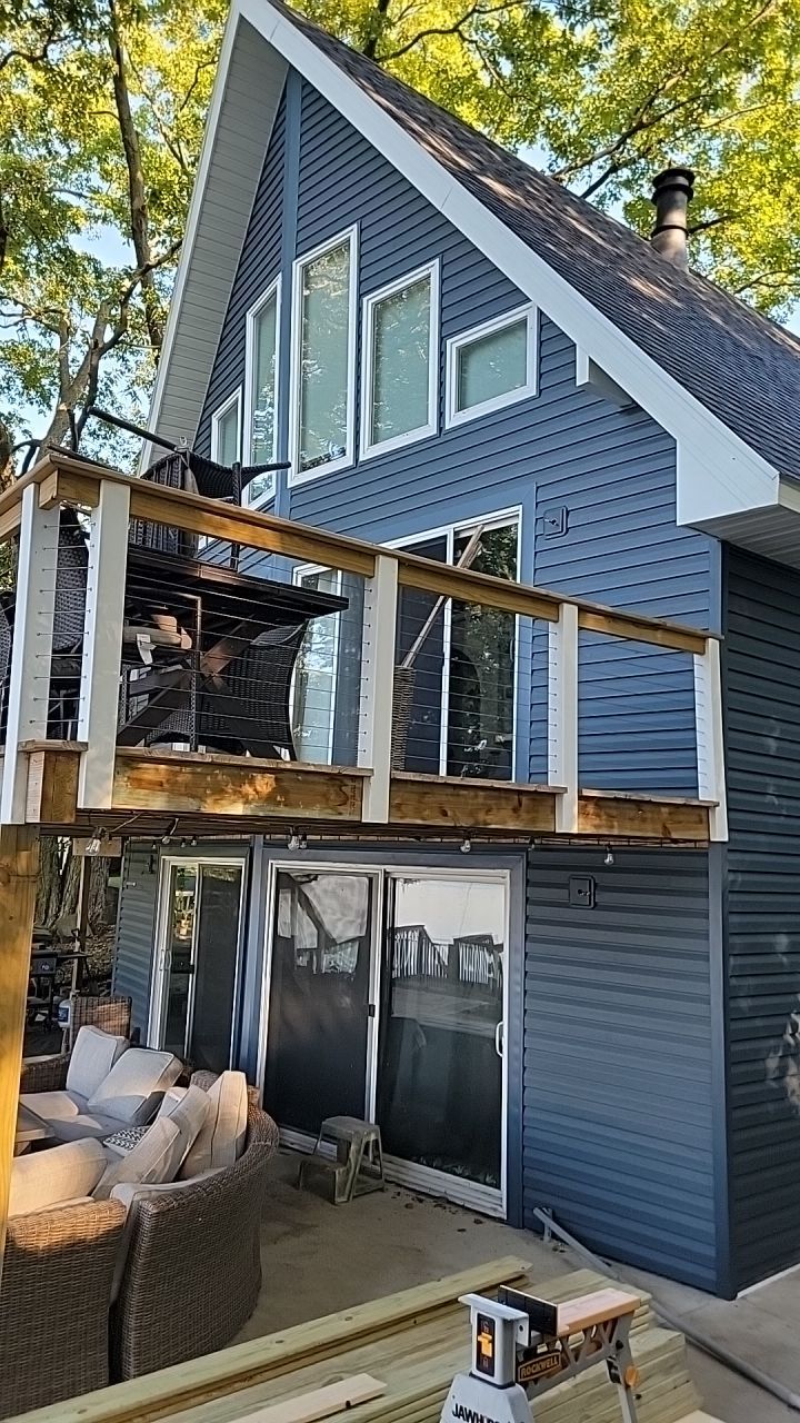 A blue A-frame house with a wooden deck and sliding glass doors, nestled among trees.