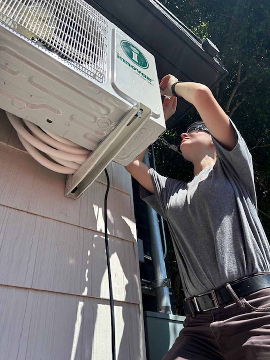 Technician working on an outdoor air conditioner unit mounted on a building wall