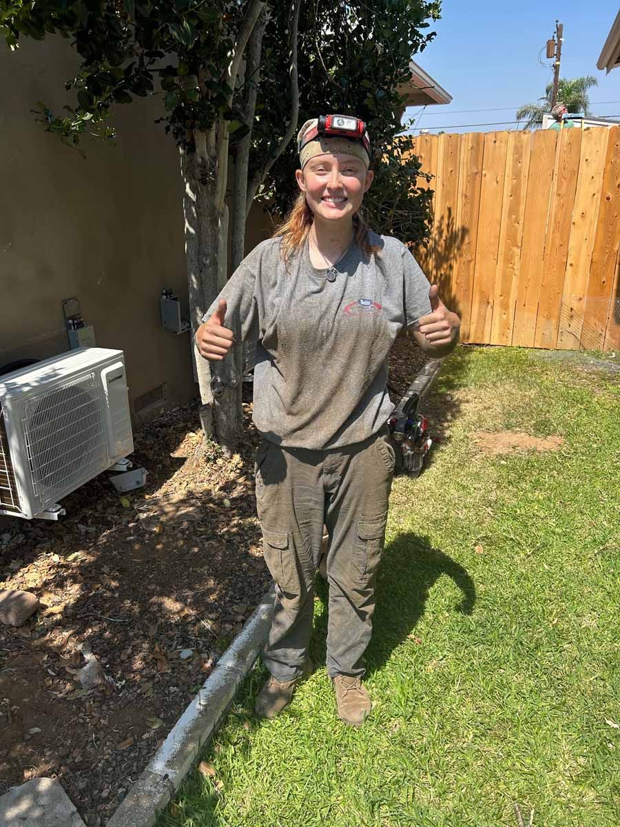 Person standing on a grassy lawn holding gardening tools, with a fence and trees in the background.