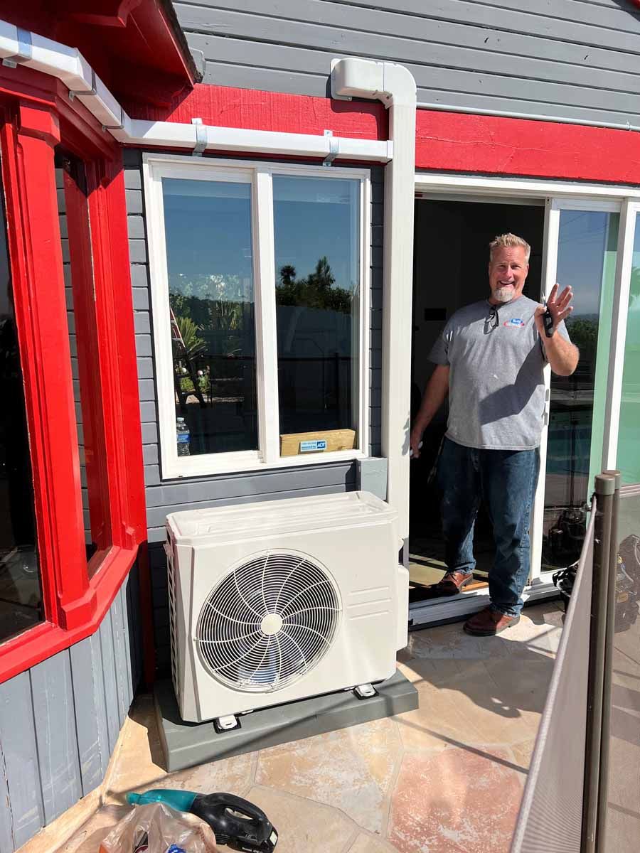 Man standing on a rooftop balcony beside a white air-conditioning unit, holding up two fingers.