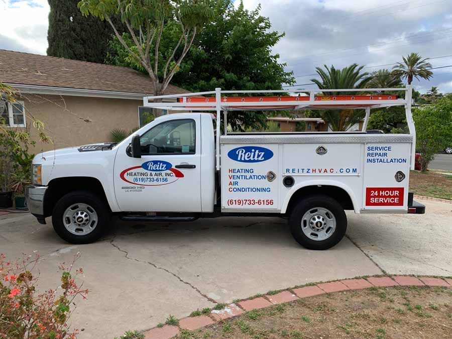 White service truck with ladders parked in a driveway outside a house