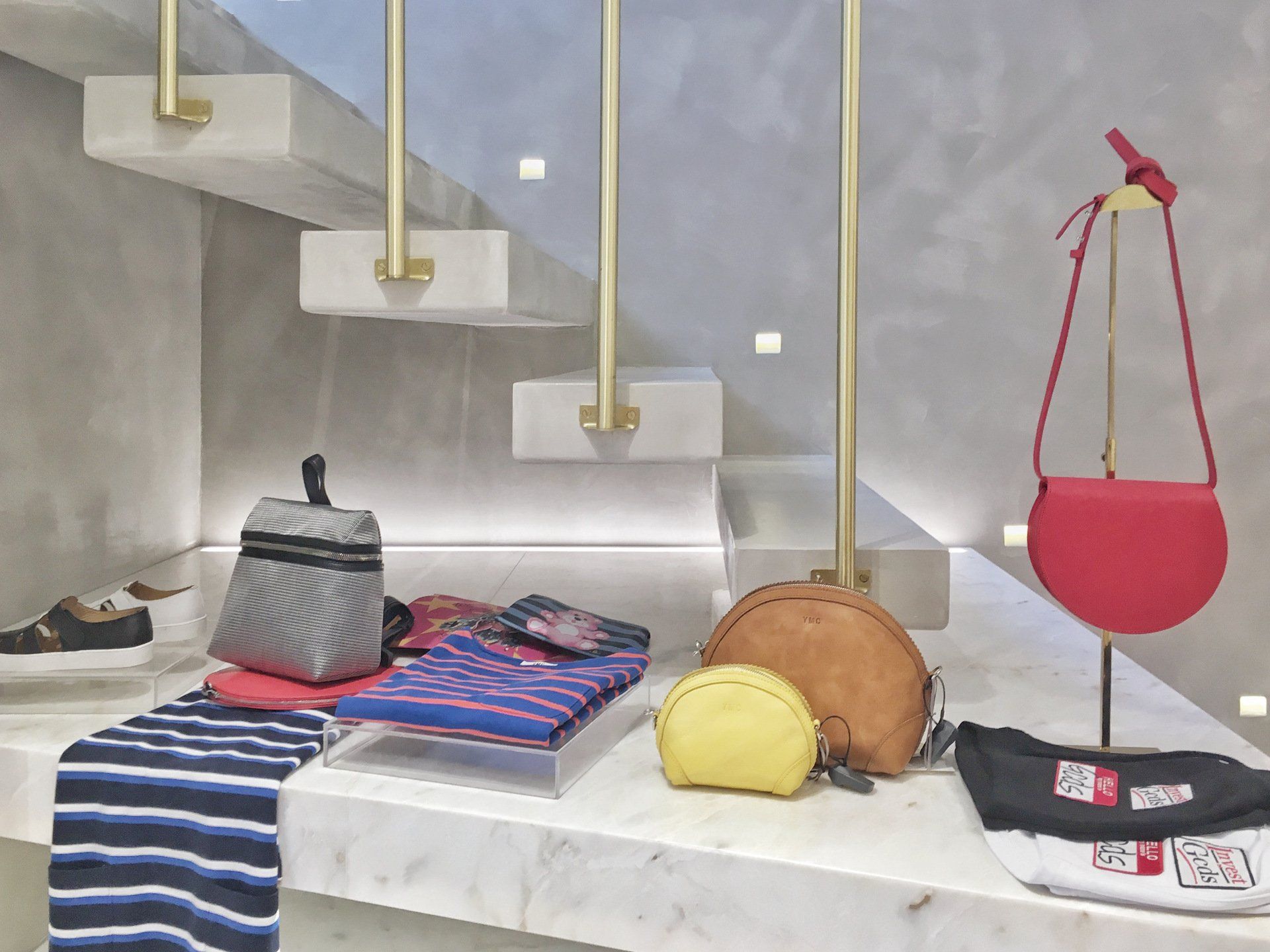Display of handbags, accessories, and clothing on a marble shelf. Includes a red crossbody bag and stairs.