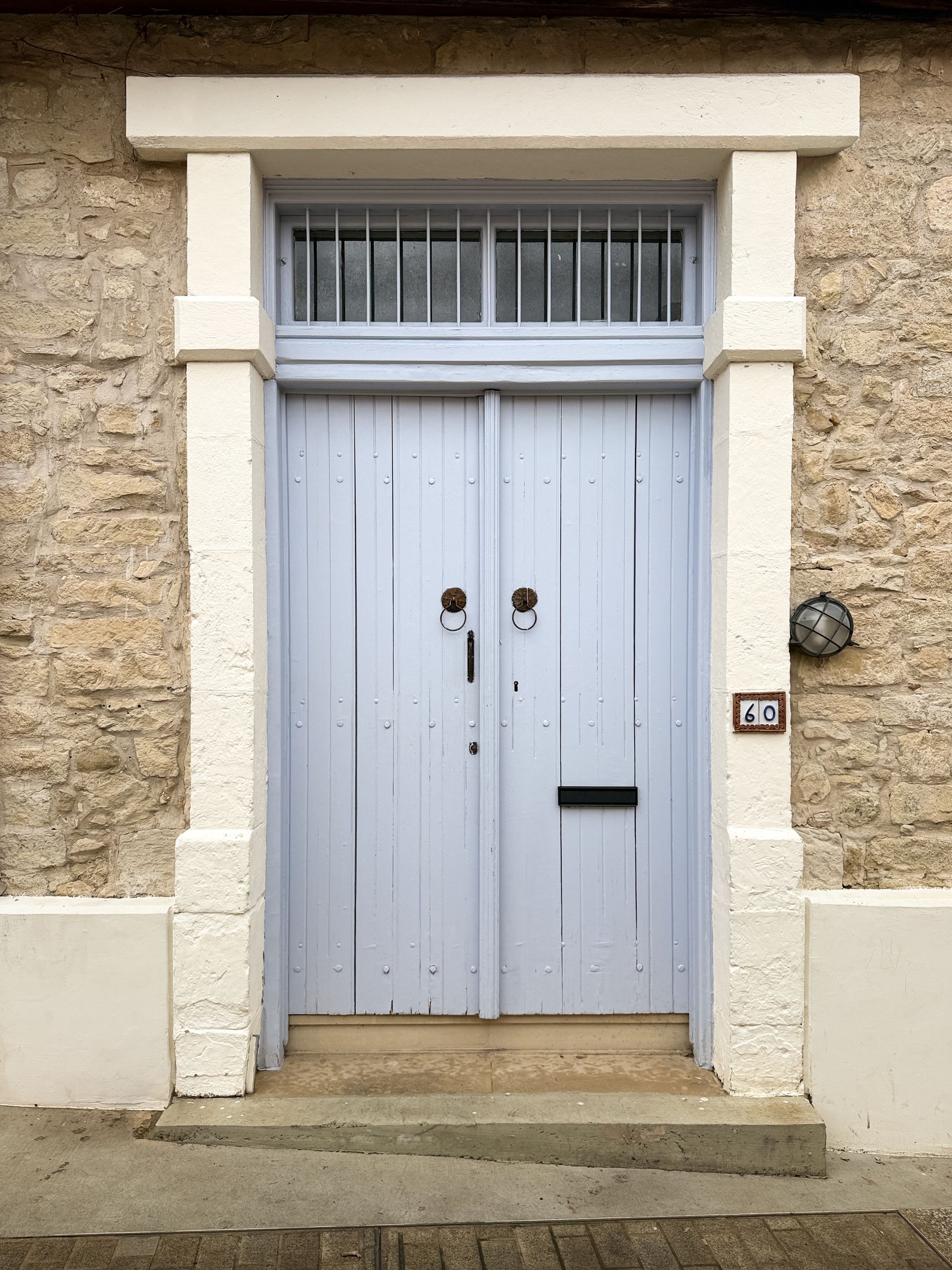 White wooden double doors with a barred transom set in a stone wall, with steps leading up.