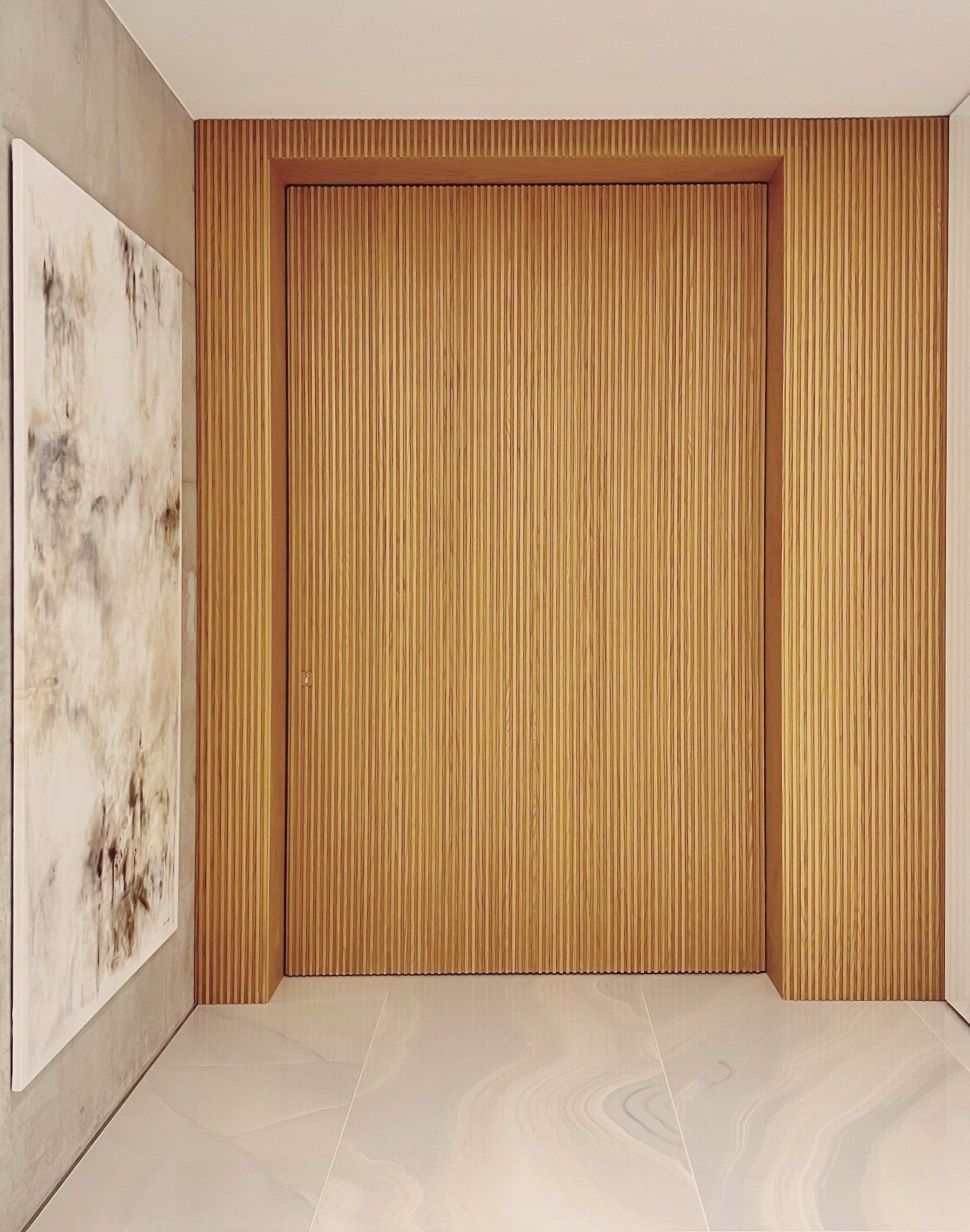 Wooden paneled door, entryway, and marble artwork. Light beige and brown tones.