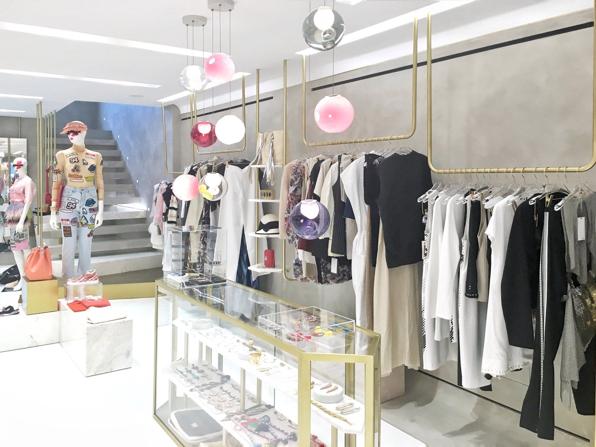 Clothing store interior with clothing racks and display case; pink, white, and gold accents.