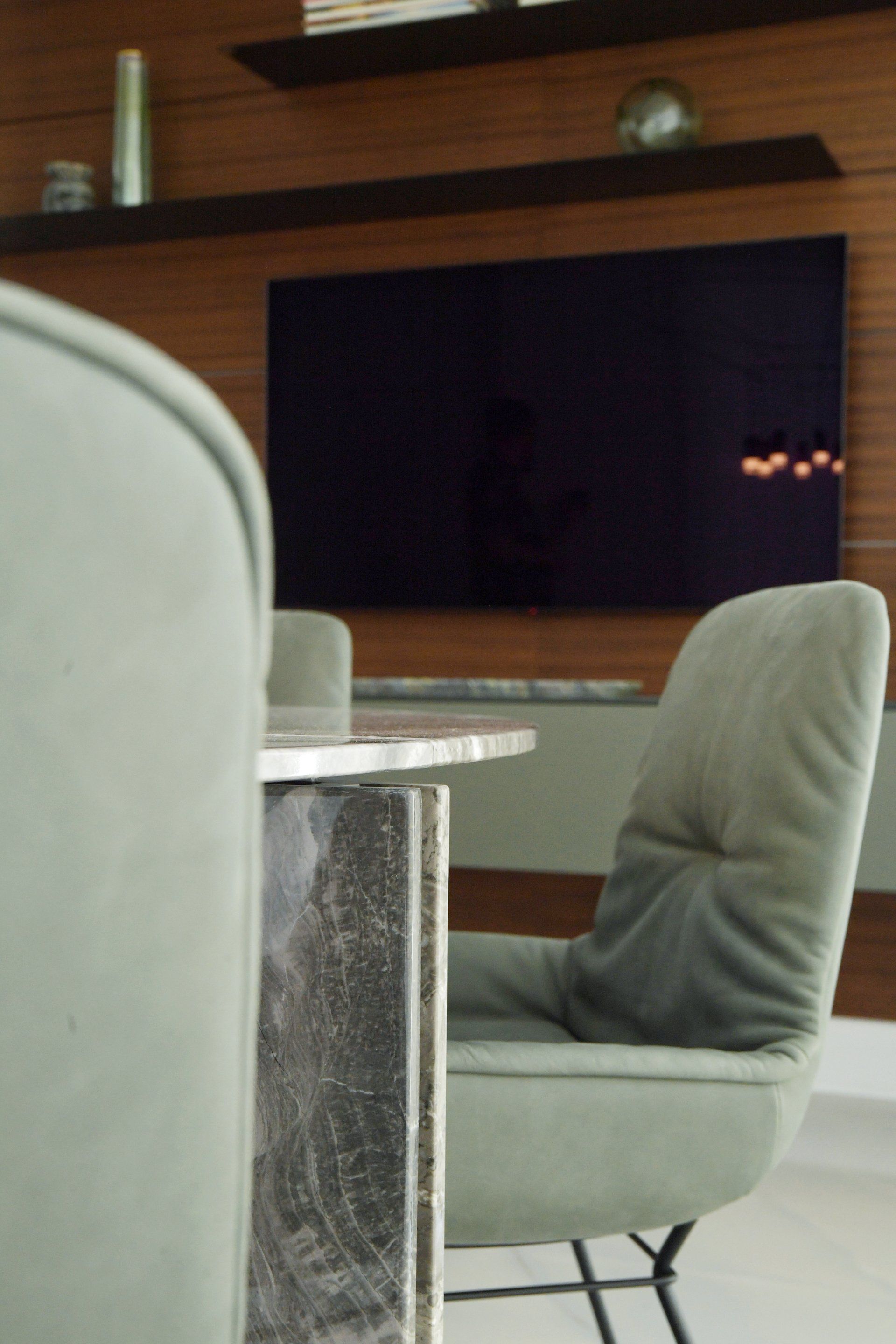 Dining table with gray upholstered chairs in front of a mounted TV on a wood-paneled wall.