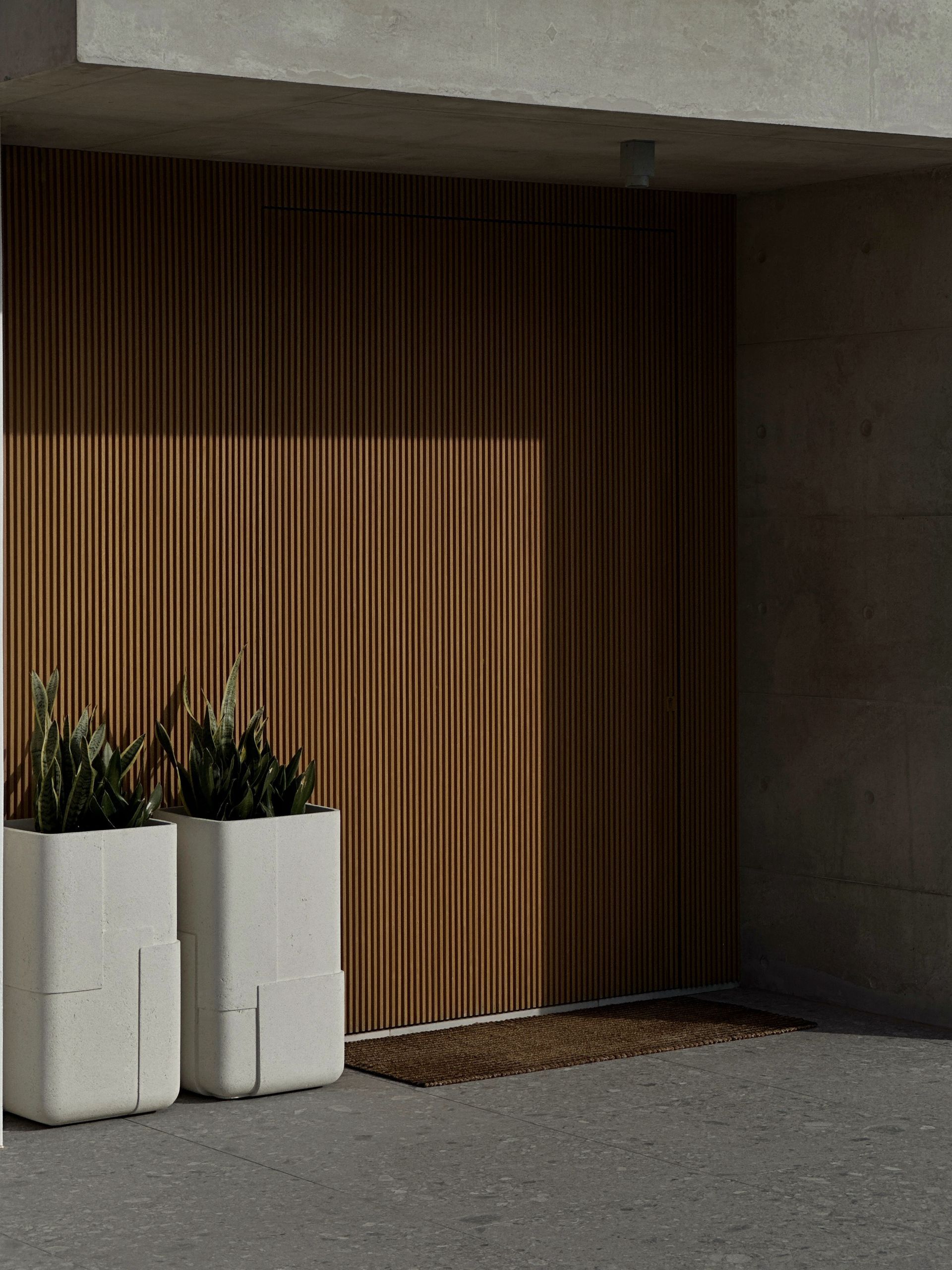 Entryway with two white planters, brown slatted wood wall, and a welcome mat.