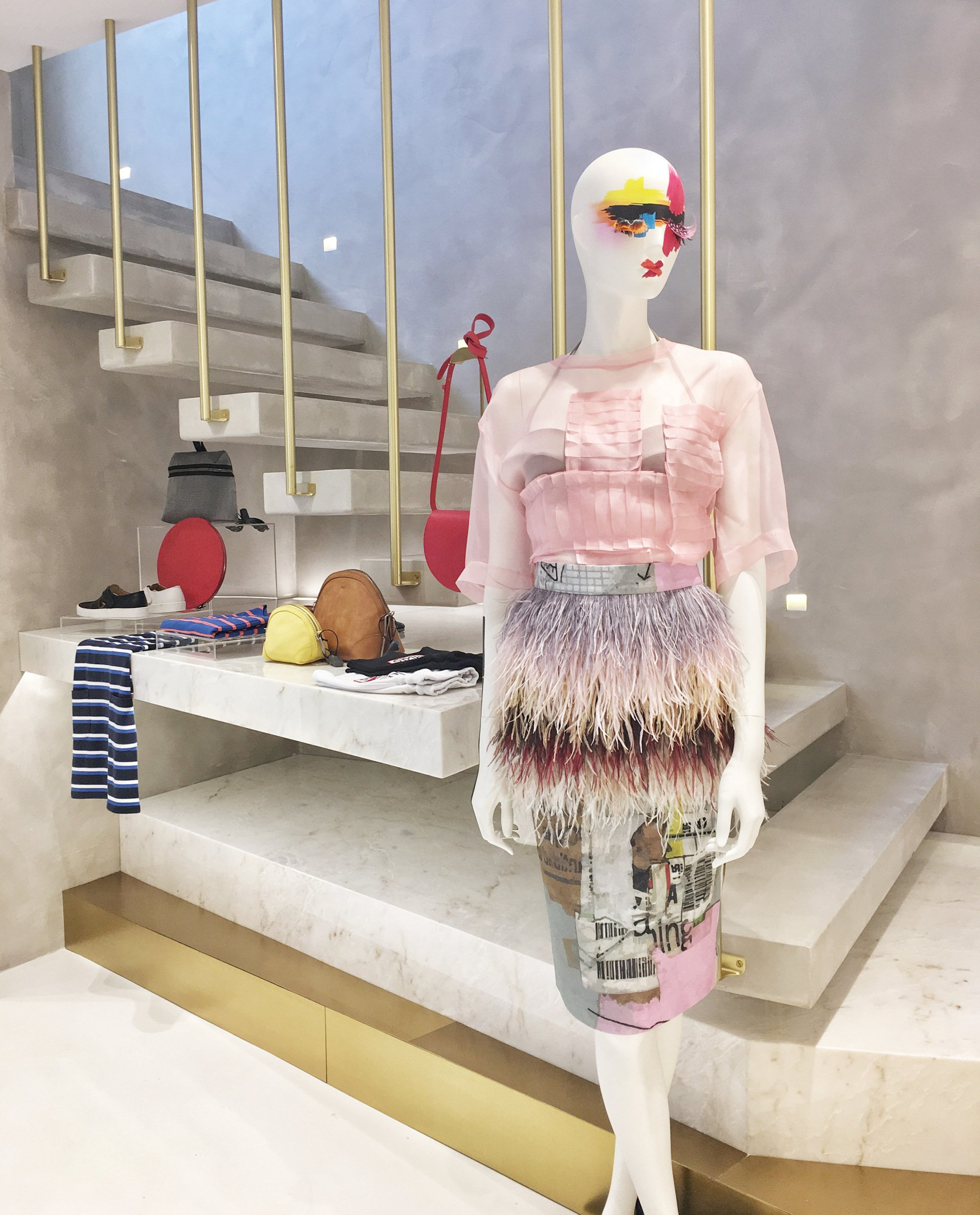 Mannequin in feathered dress, on stairs in a boutique. Accessories on display. Modern setting with gold accents.