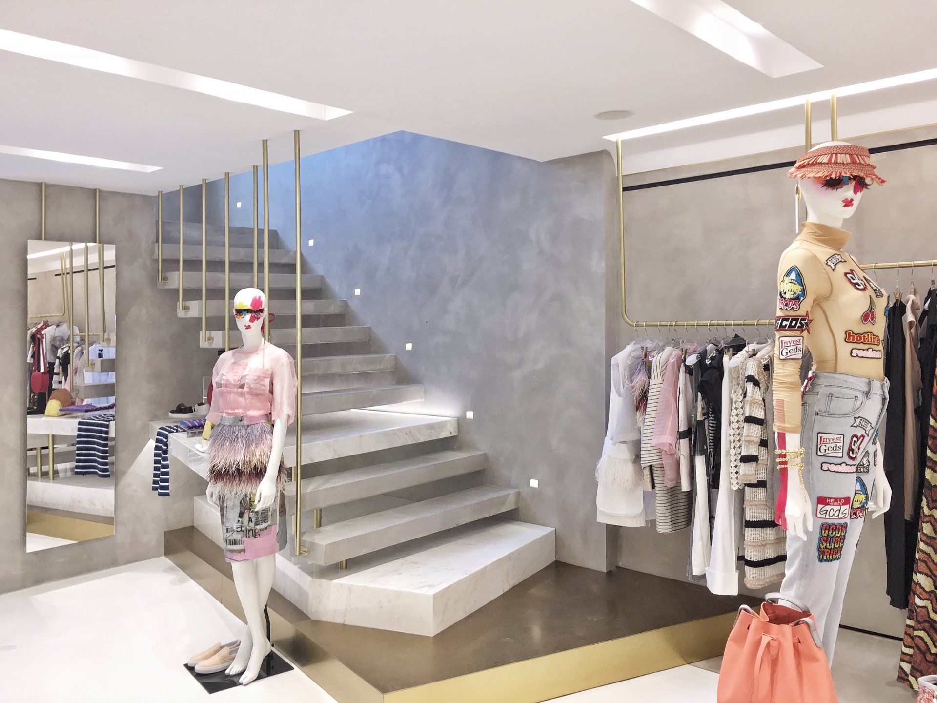 Clothing store interior with mannequins on stairs, racks of clothes, and gold accents.