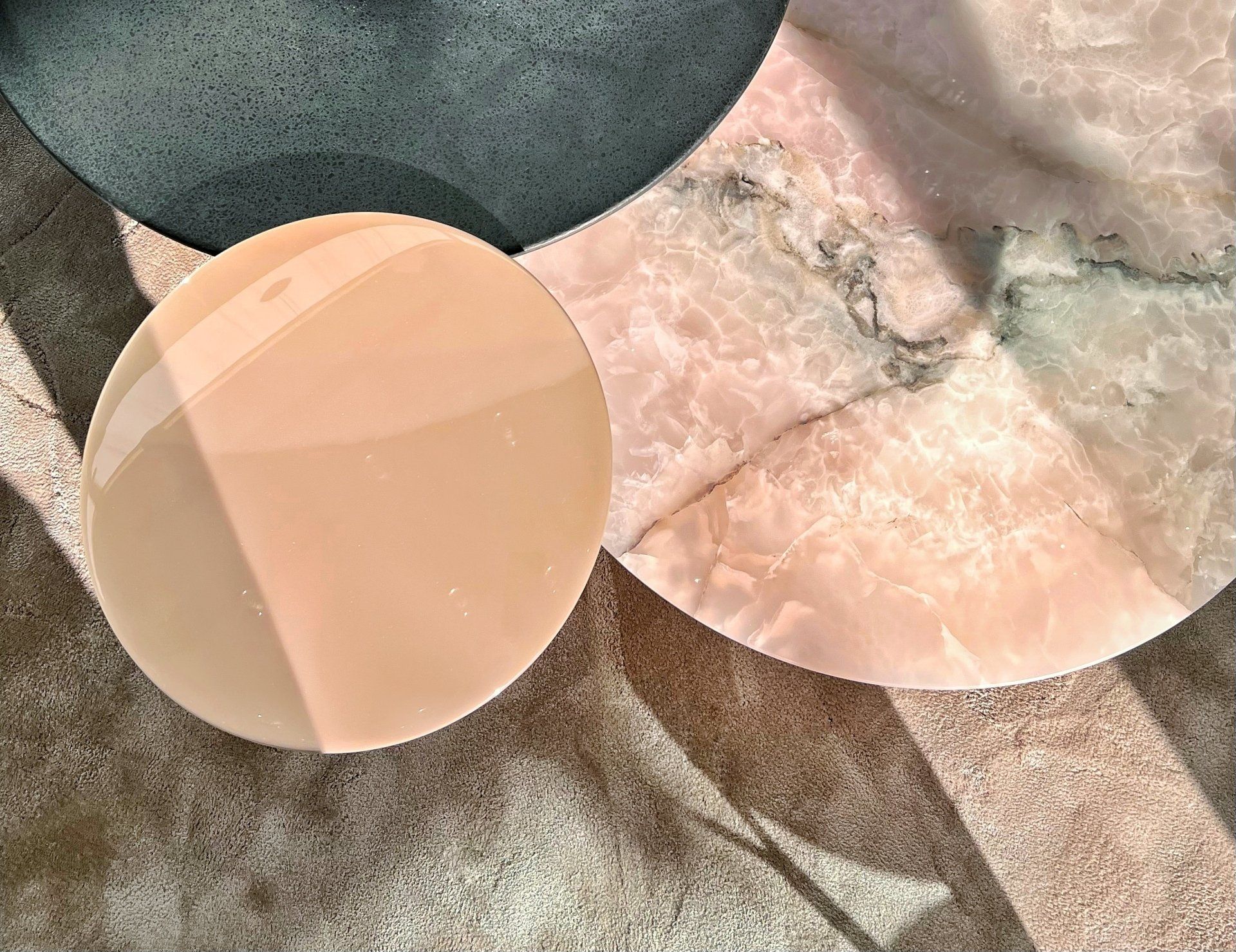 Overhead view of three circular tabletops: pink marble, dark gray, and peach-colored.