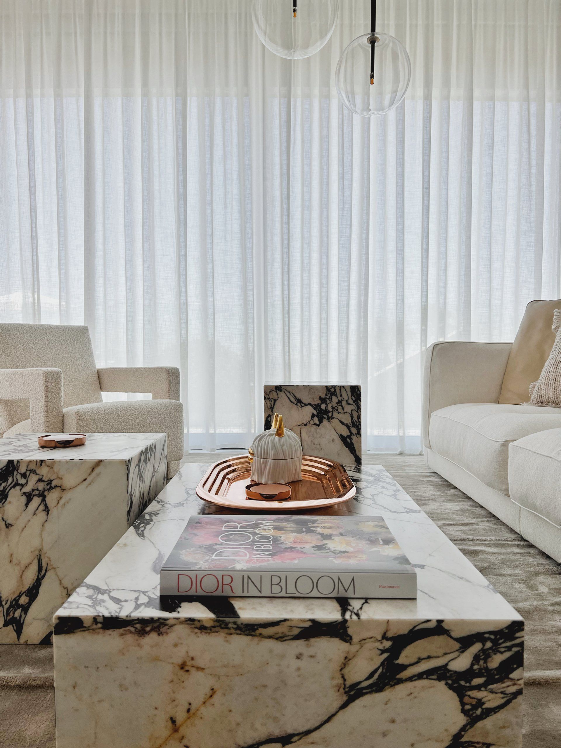 Living room with marble coffee table, white sofa, cream chairs, and sheer curtains.