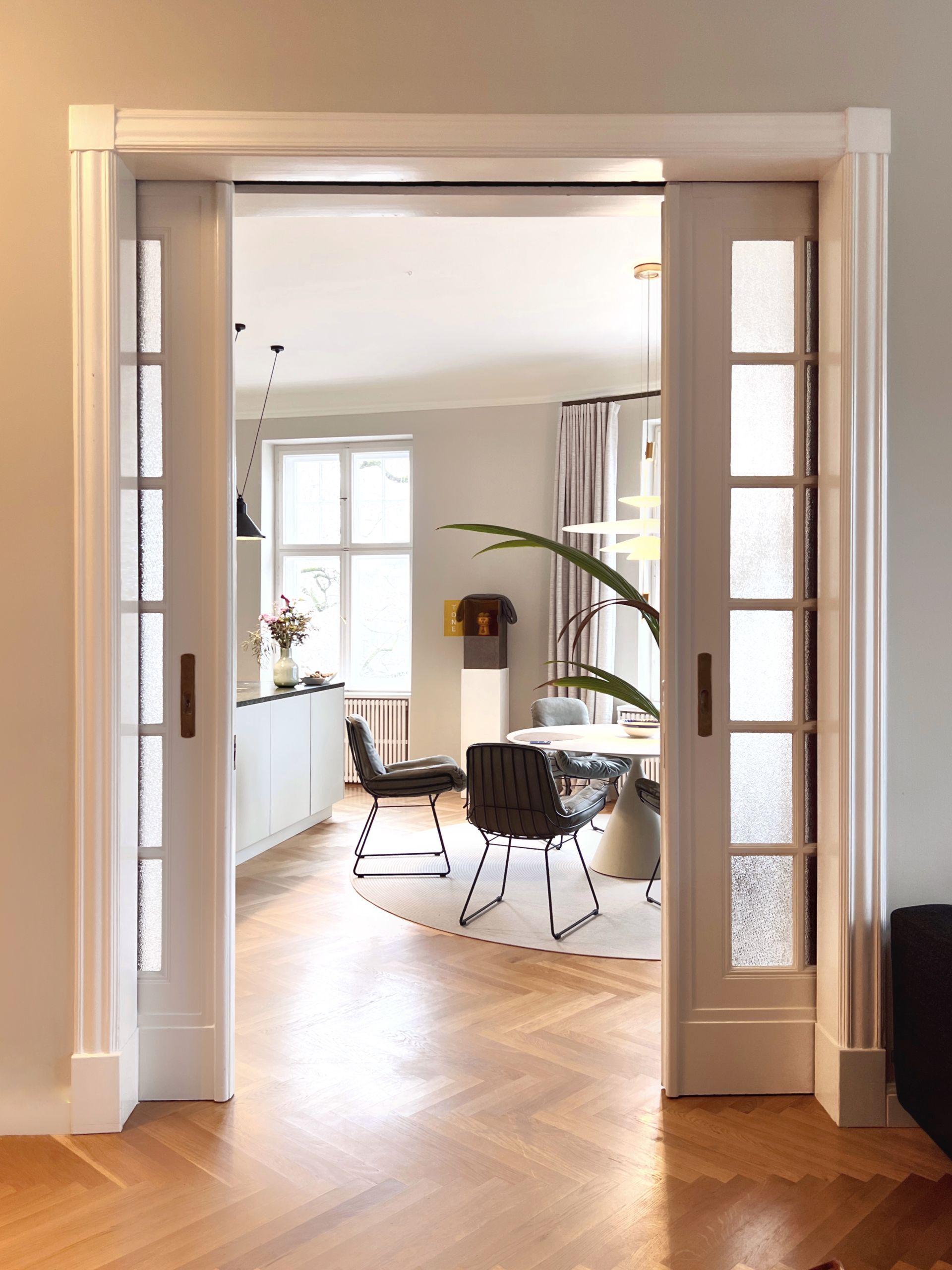 Long hallway with glass table, flowers, checkered rug, and modern light fixture.