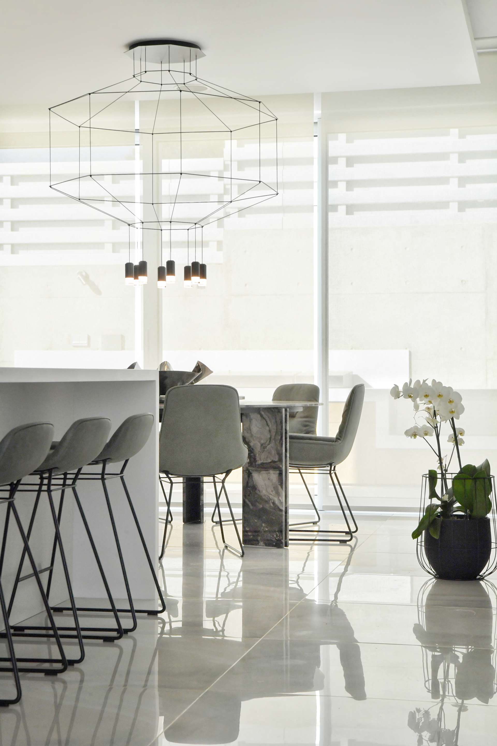 Modern kitchen room with bar stools, gray chairs, a geometric light fixture, and reflective floors.