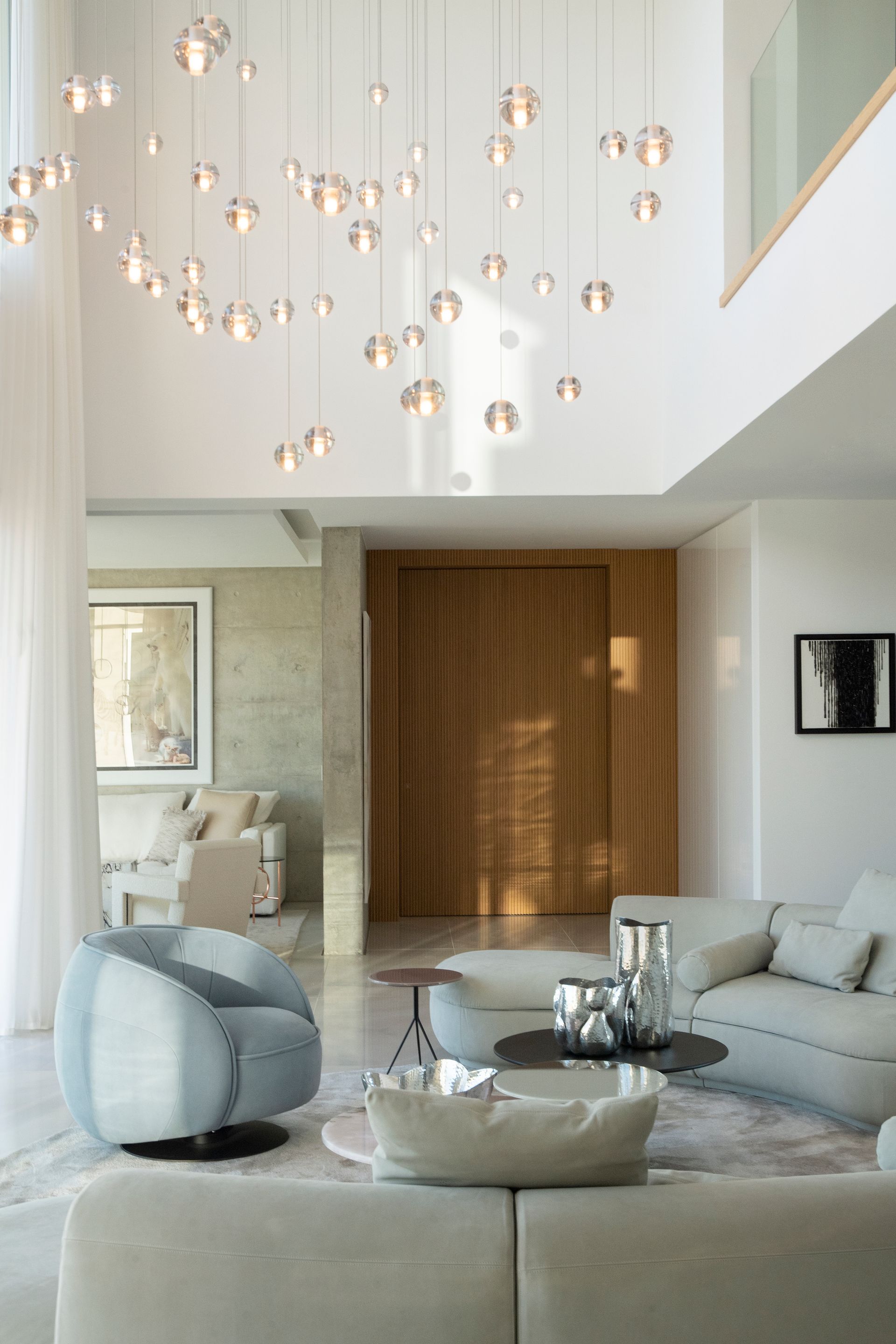 Living room with light-colored furniture, wooden door, and a large cluster of spherical hanging lights.