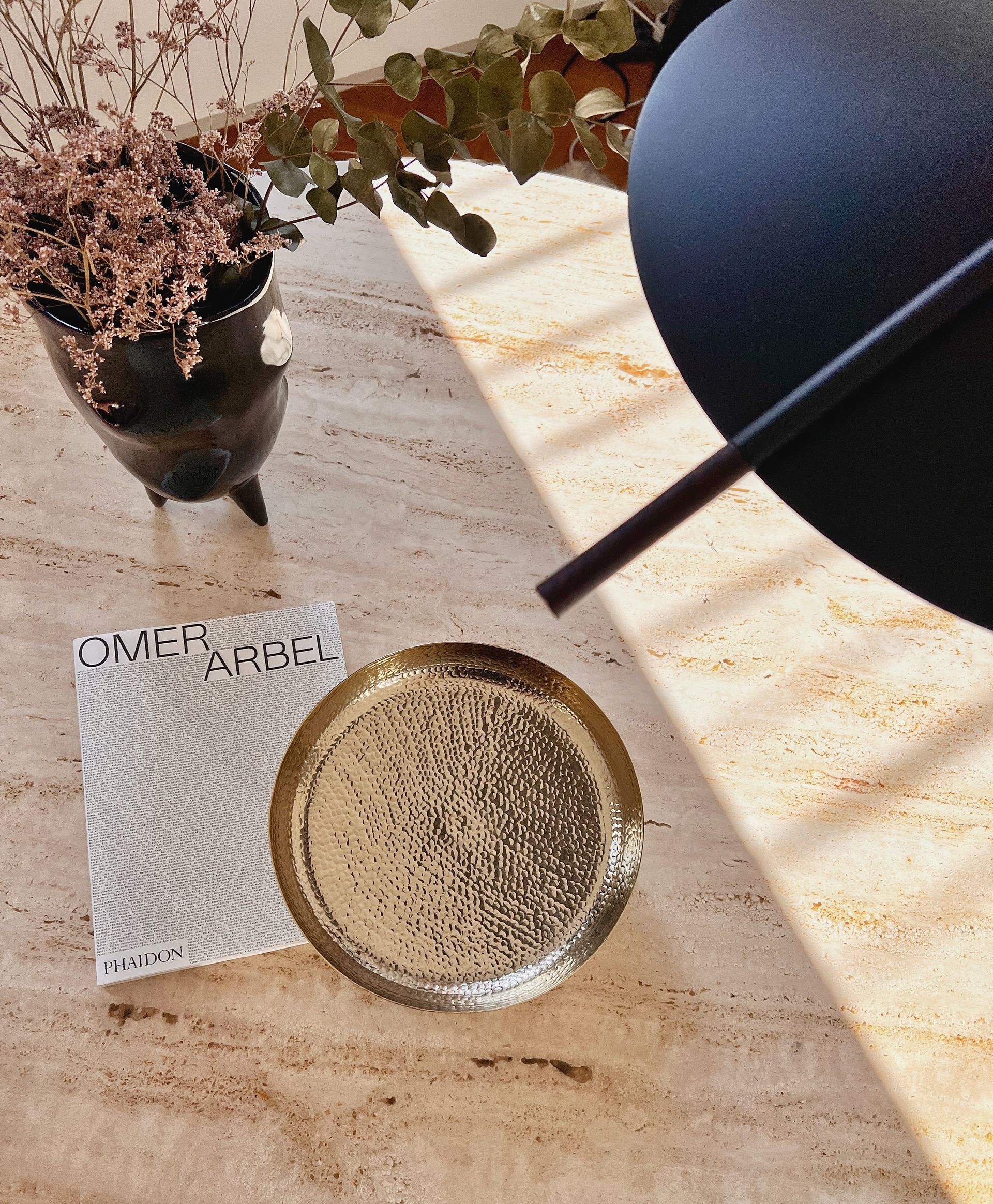 Gold tray, book, black object, and potted plant on a travertine marble surface.