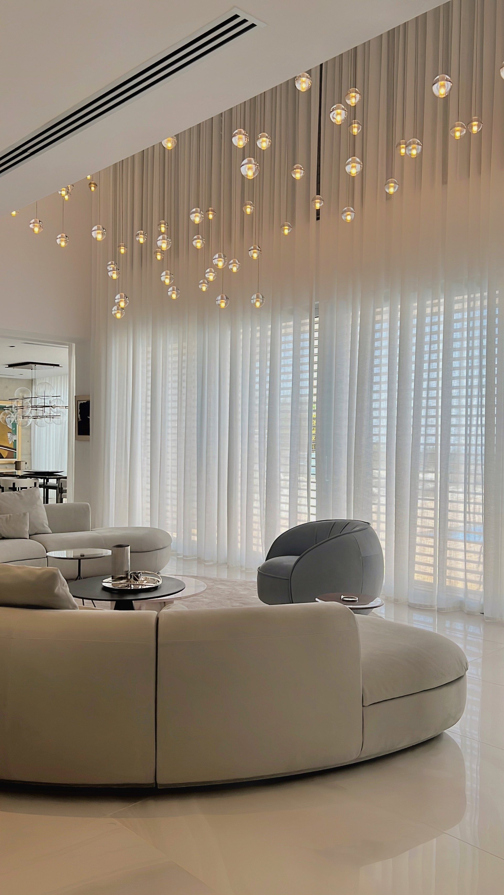 Modern living room with a circular couch, sheer curtains, and a multi-light chandelier.