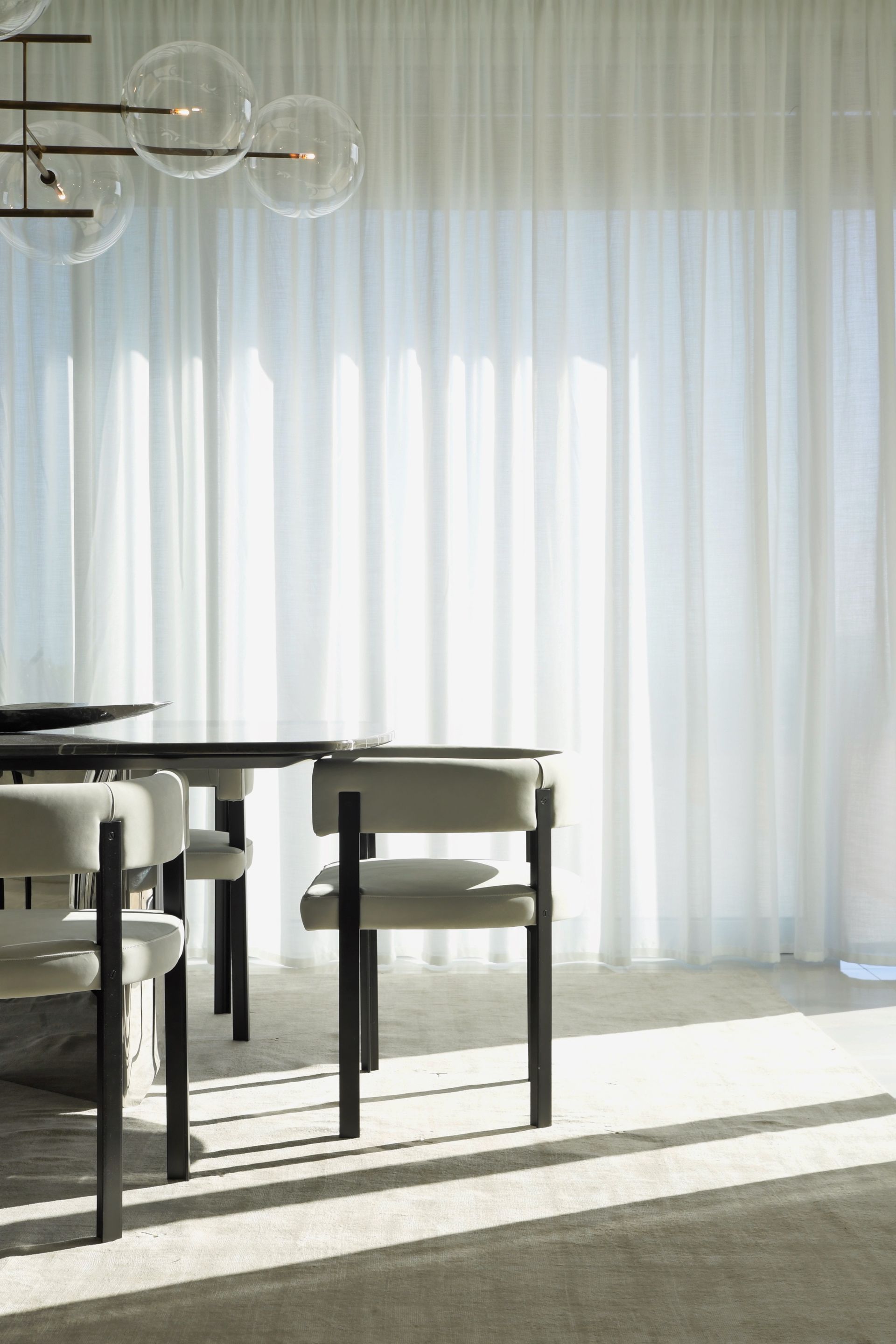 Dining room with a black table, chairs, sheer curtains, and a bubble chandelier.