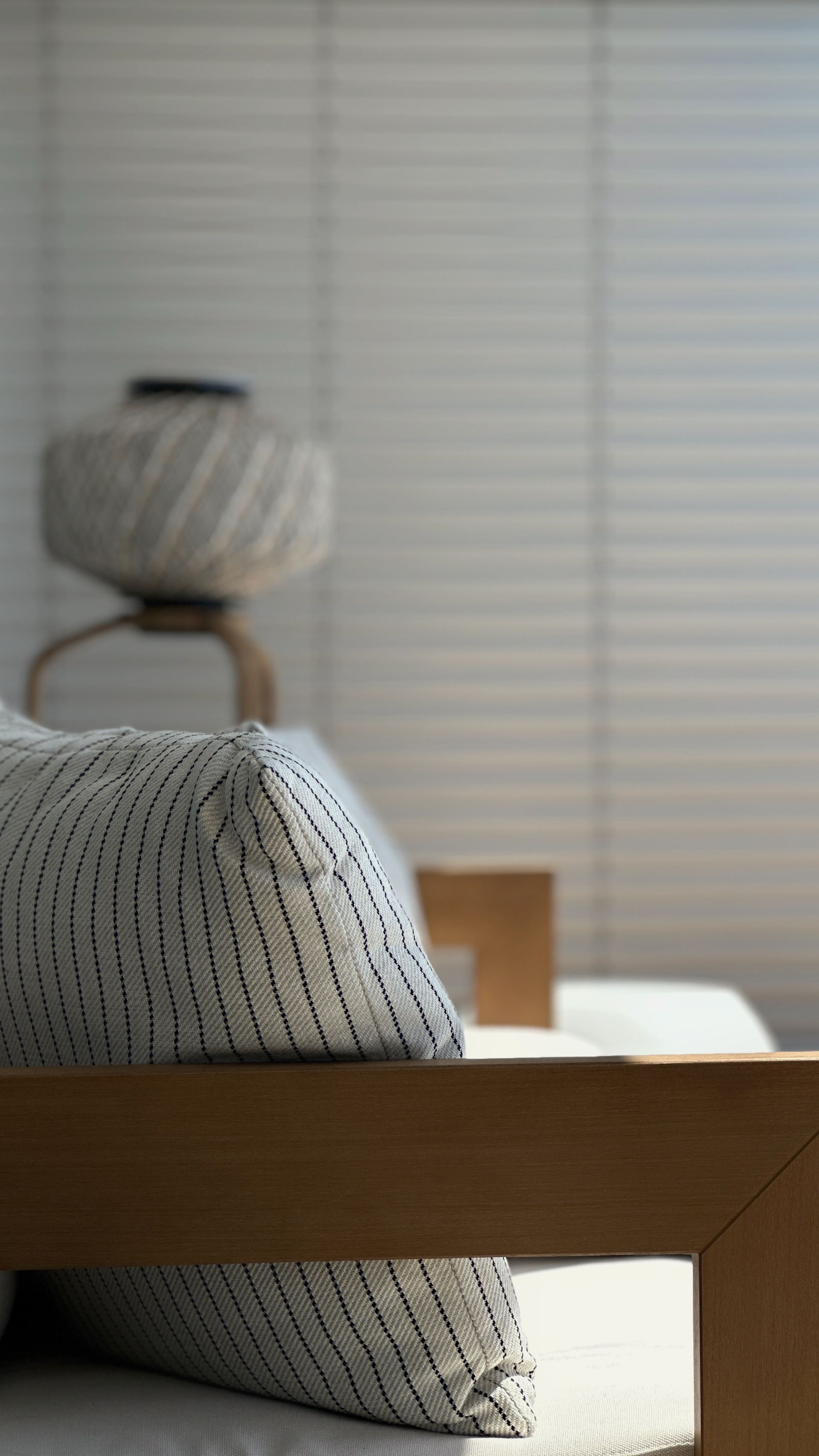 Wooden sofa frame with decor cushions, a lamp, and a window with blinds.