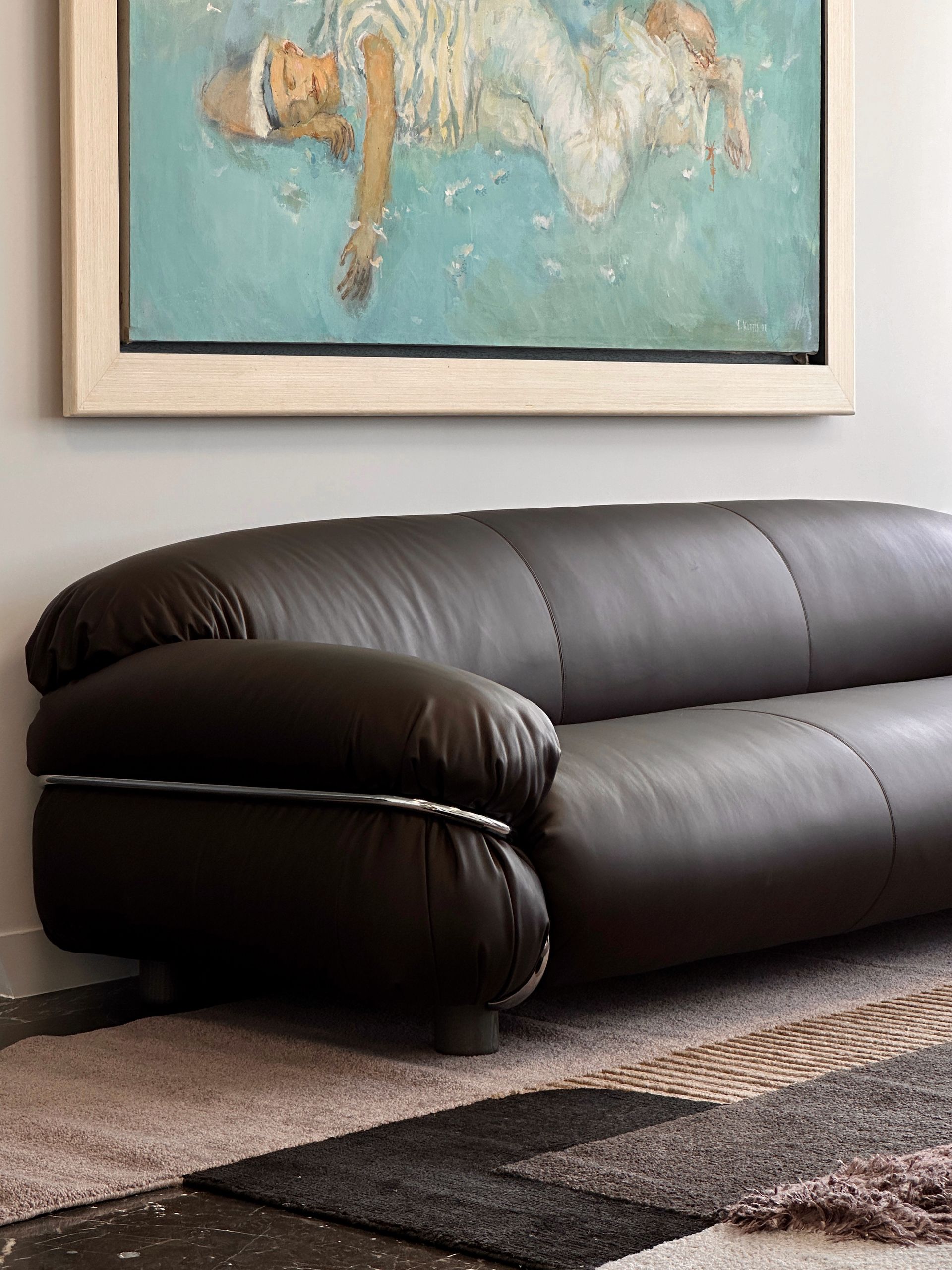 Luxurious dark leather sofa beneath a painting, set on a rug with neutral tones.