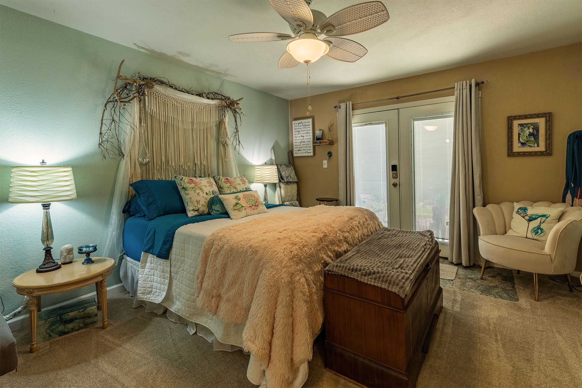 Bedroom with bed, trunk, armchair, and French doors. Light blue and beige color scheme.