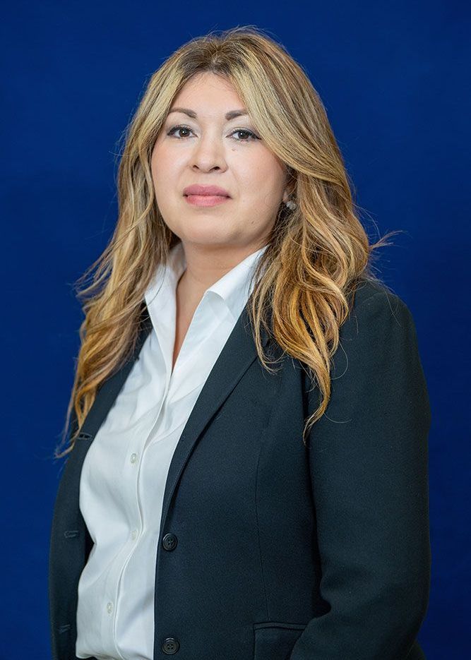Una mujer con traje y camisa blanca está parada frente a un fondo azul.