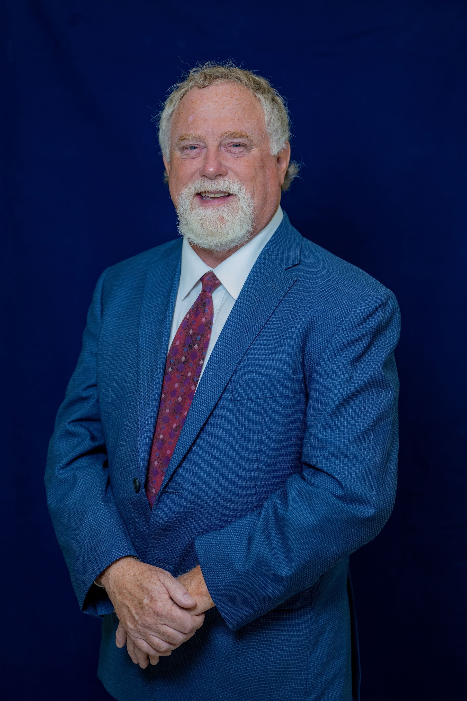 Un hombre con traje y corbata está de pie delante de un fondo azul.