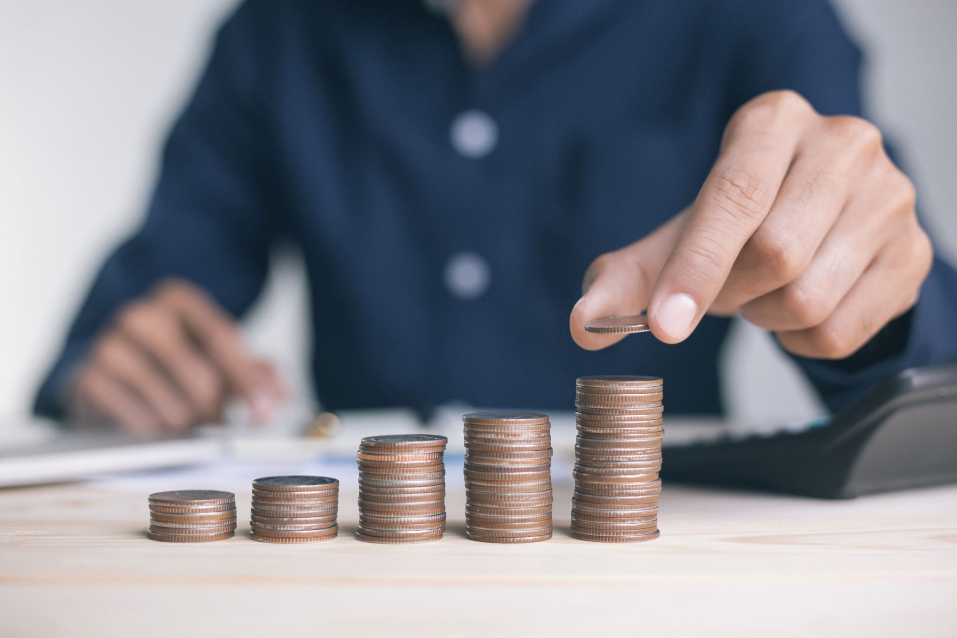 Person stacking coins, creating a rising graph; financial concept.