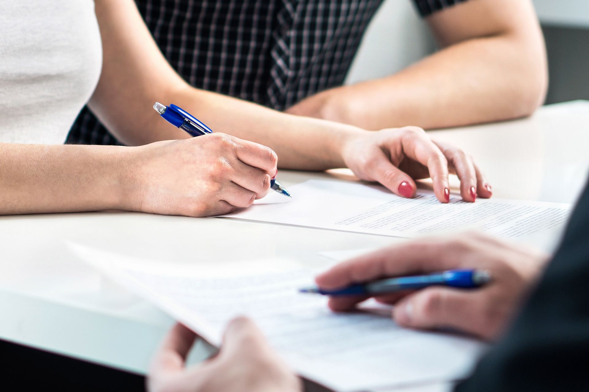 Hands signing a document with blue pens at a white table.