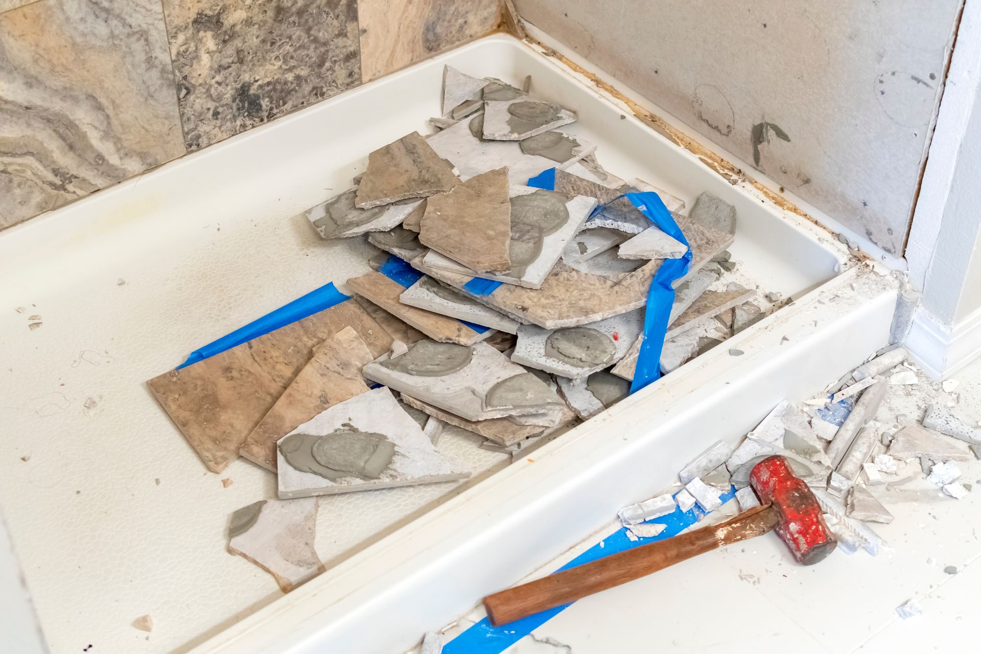 A hammer is sitting on top of a pile of tiles in a shower stall.