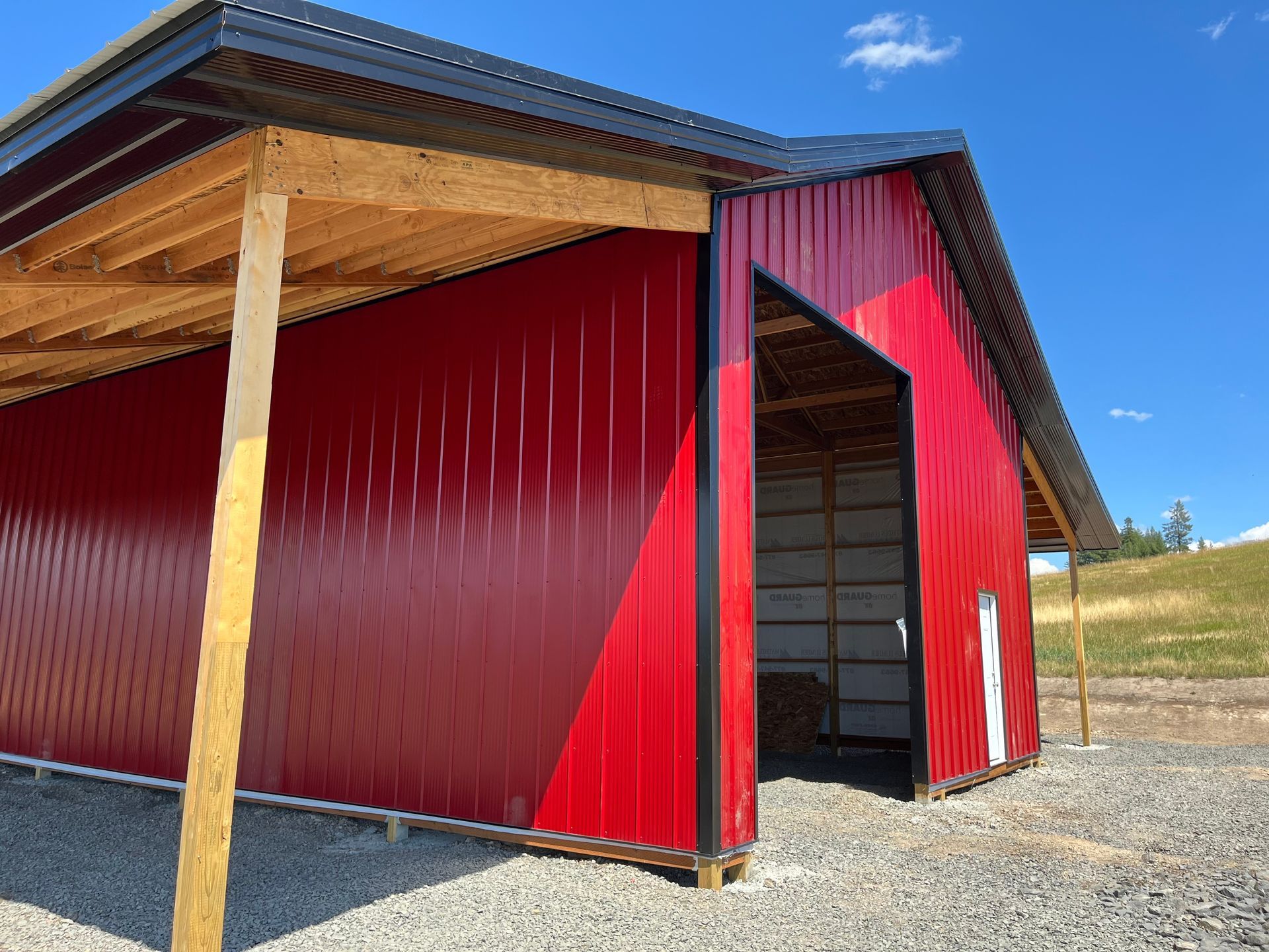 A red barn with a wooden roof is sitting on top of a gravel lot.