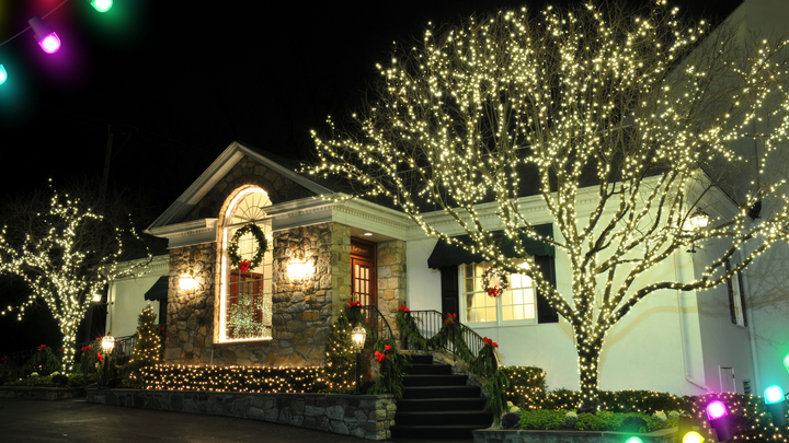 House with trees adorned with twinkling Christmas lights. Festive wreaths and garland decorate the entrance.