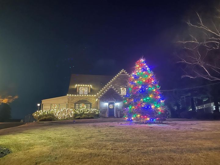 House and Christmas tree illuminated with colorful lights at night.