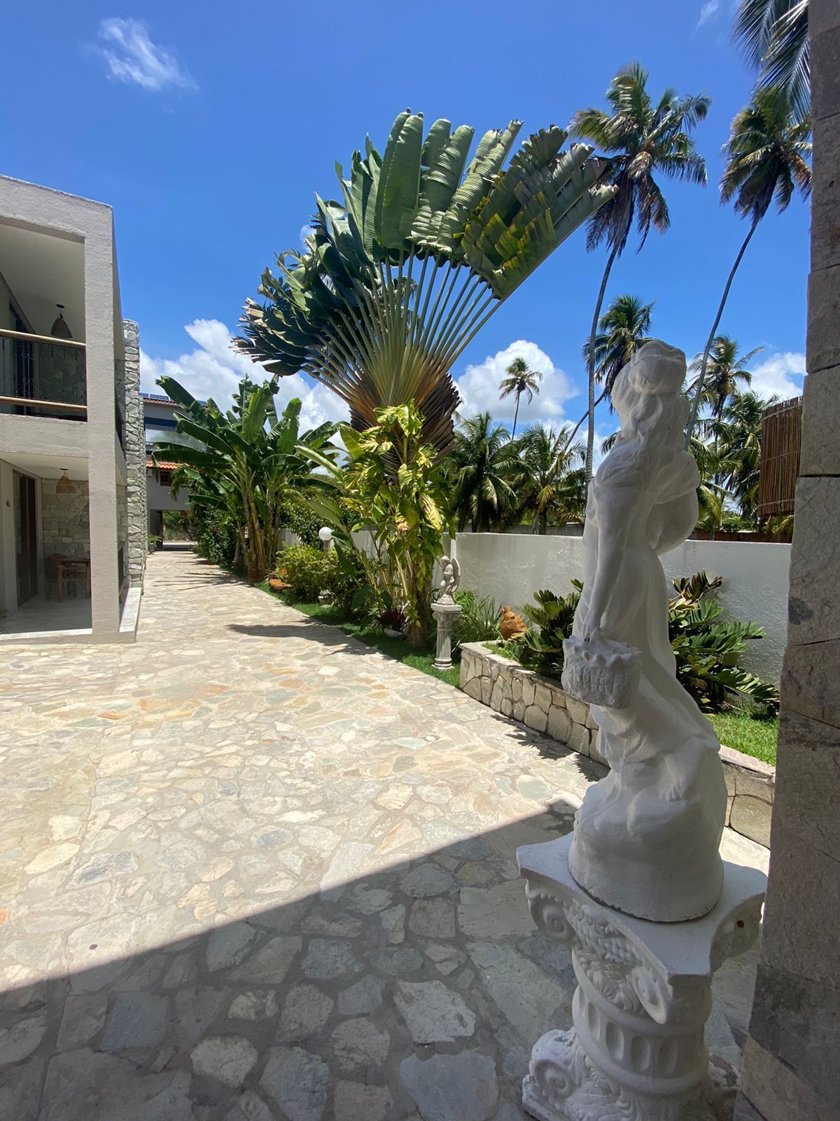 Pátio com estátua, vegetação tropical e um edifício branco sob um céu azul brilhante.Pousada Villa Italiana