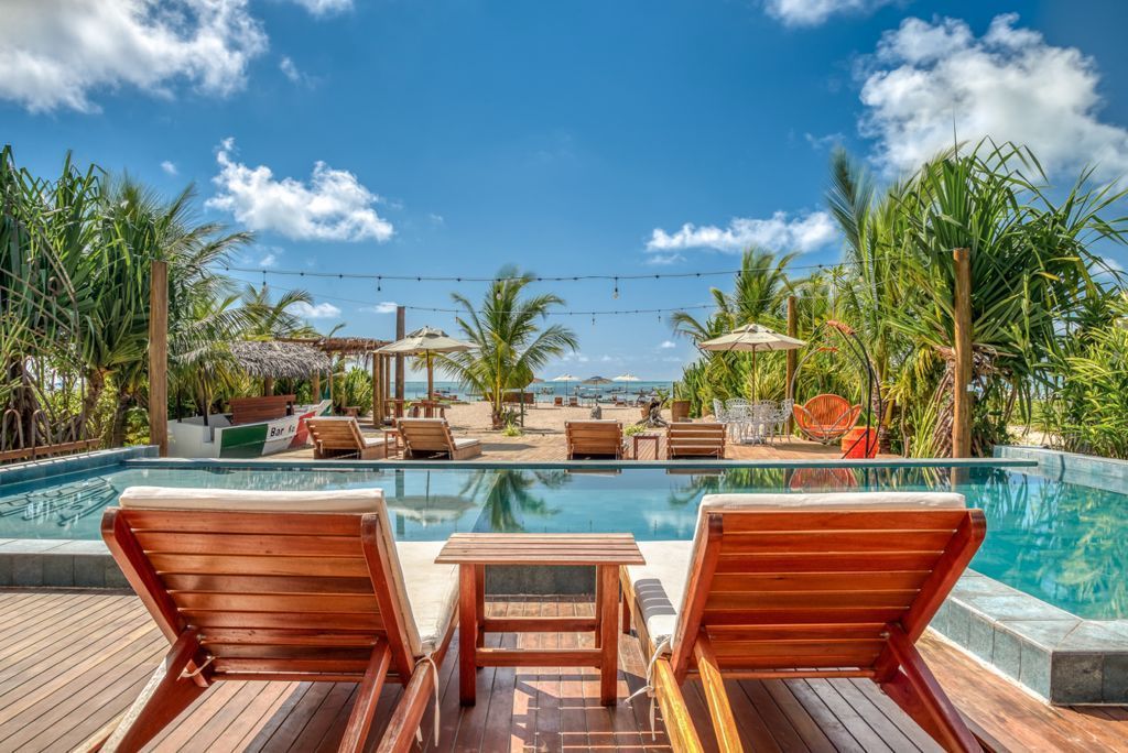 Vista para a piscina com espreguiçadeiras, piscina, praia, palmeiras e céu azul.Pousada Villa Italiana